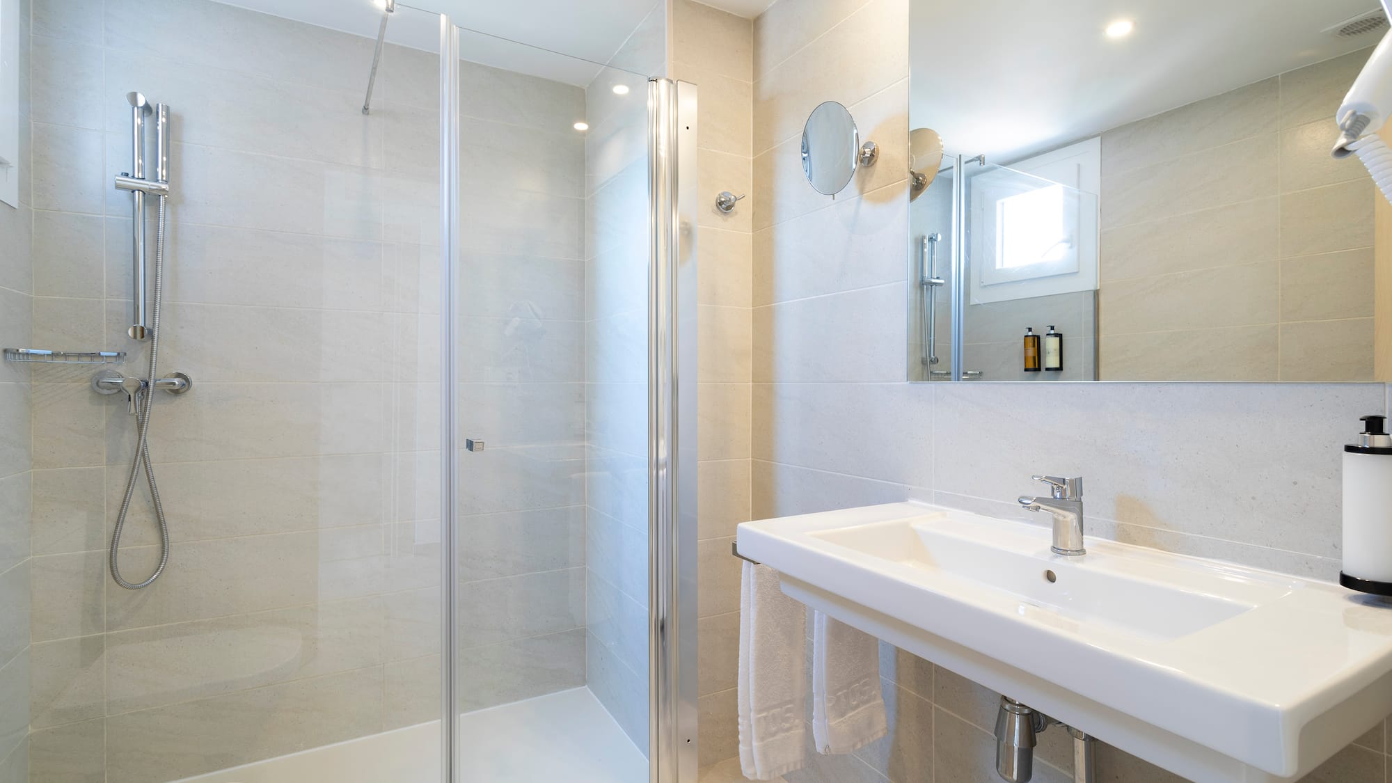 Modern tiled bathroom with glass shower, white sink, and mirror.