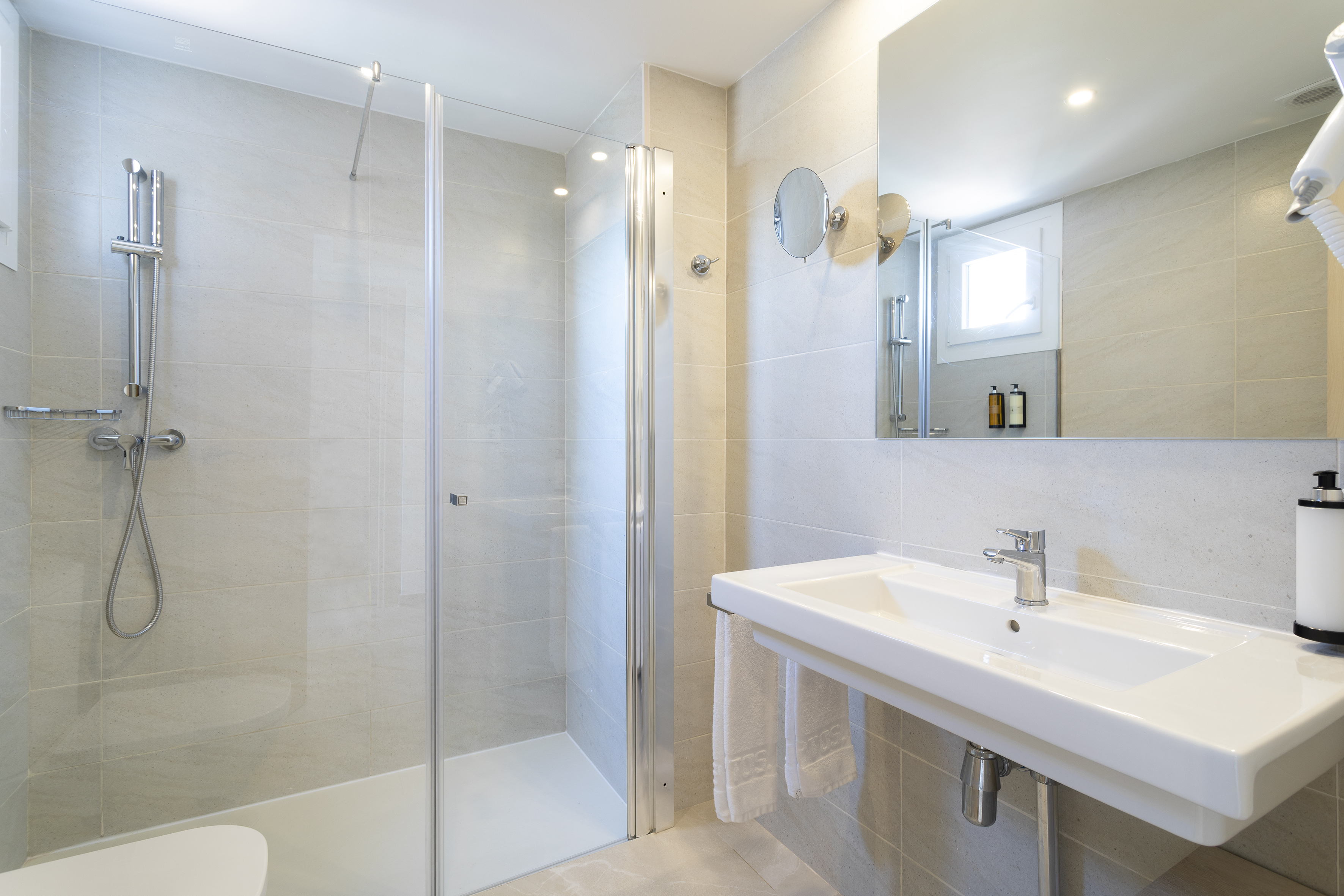 Modern tiled bathroom with glass shower, white sink, and mirror.