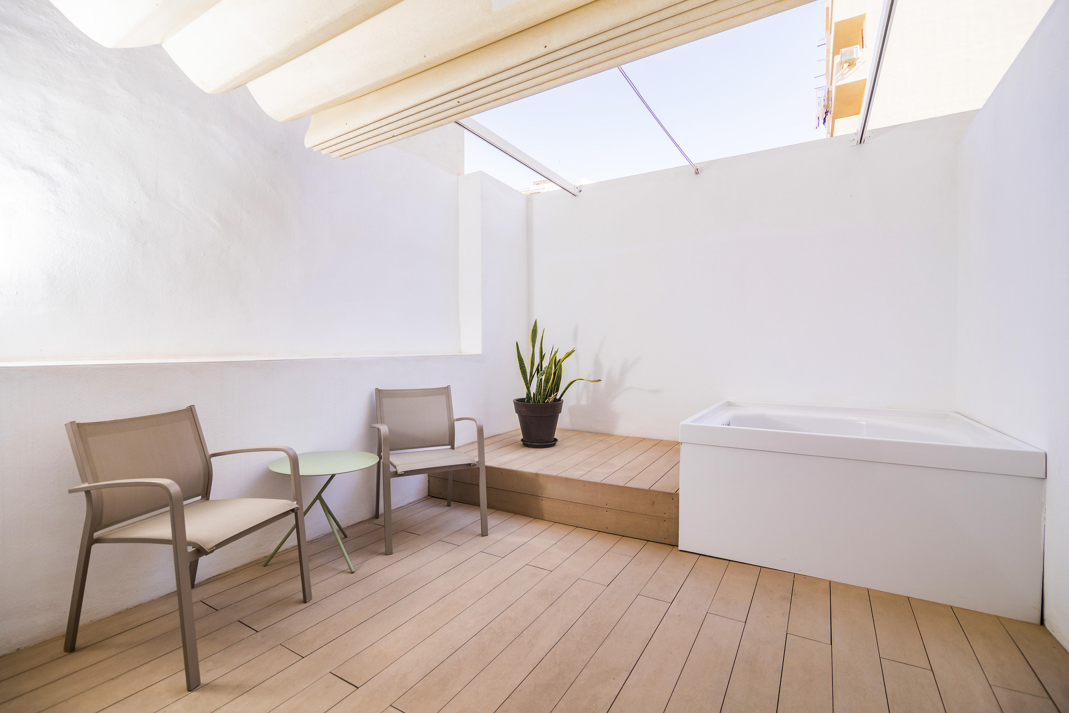 Modern outdoor patio with seating, built-in bathtub, wood floor, and plant.