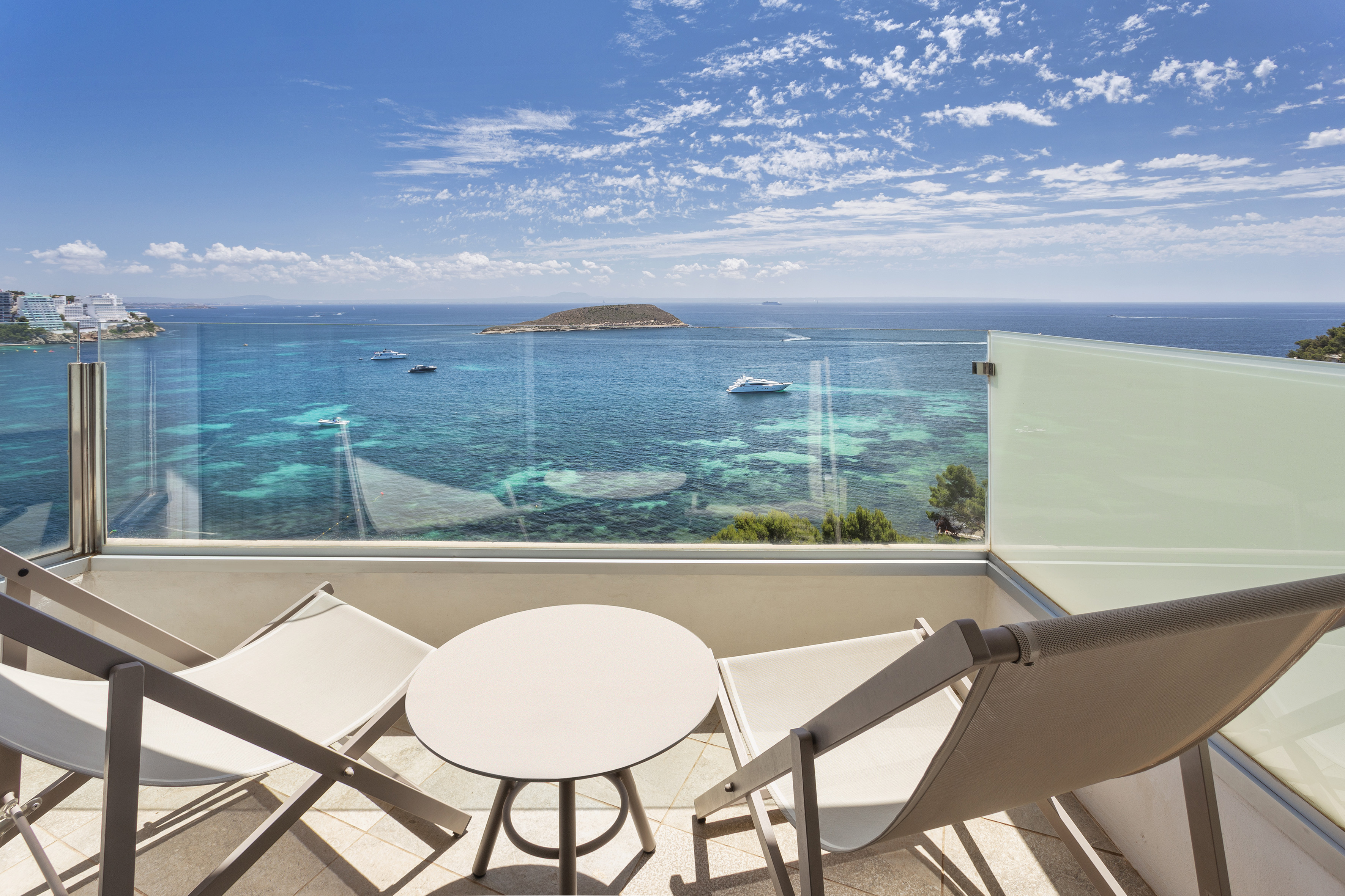 Hotel balcony with ocean view, chairs, table, yachts, and distant island.
