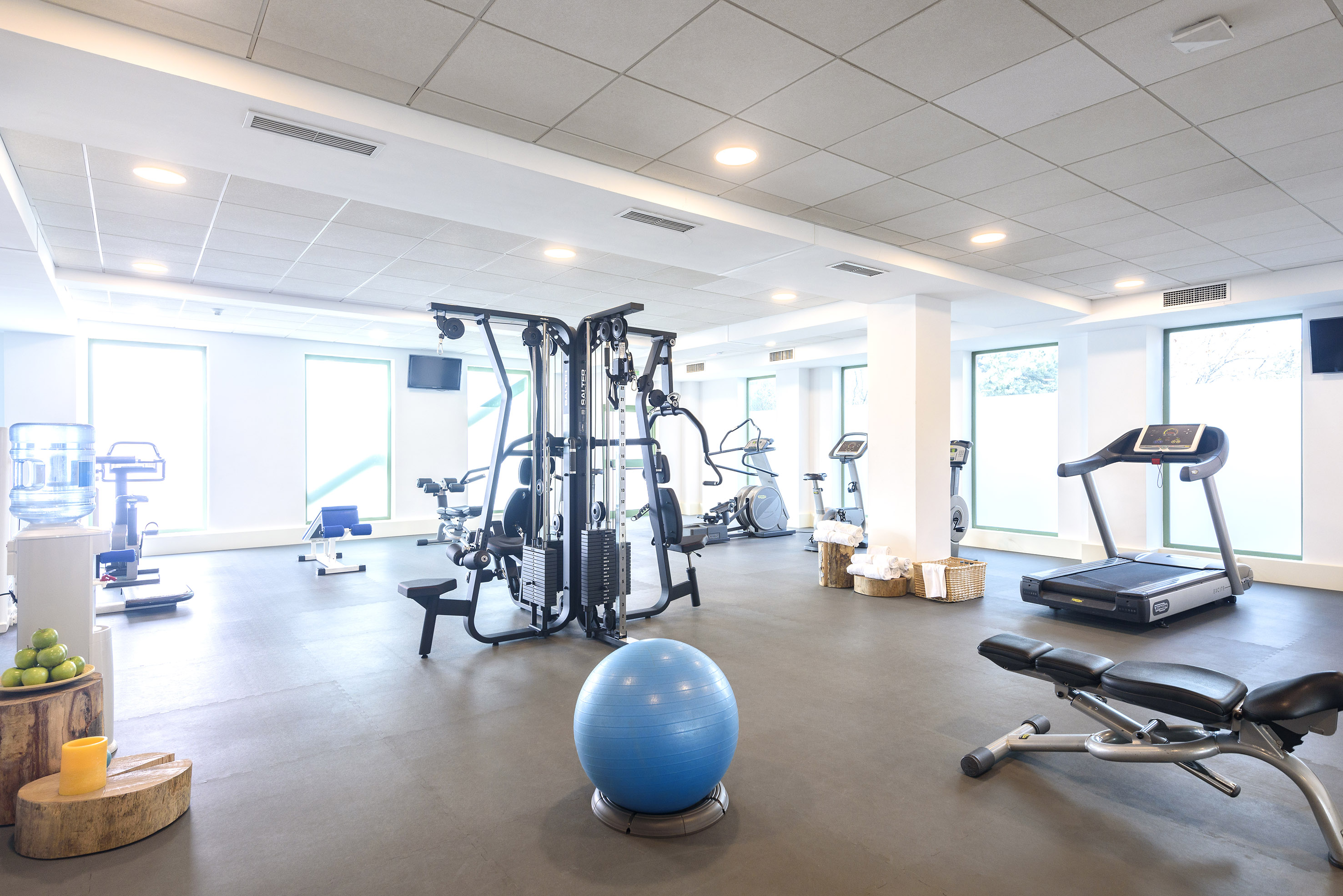 Modern hotel gym with treadmill, weight machine, and fitness ball.