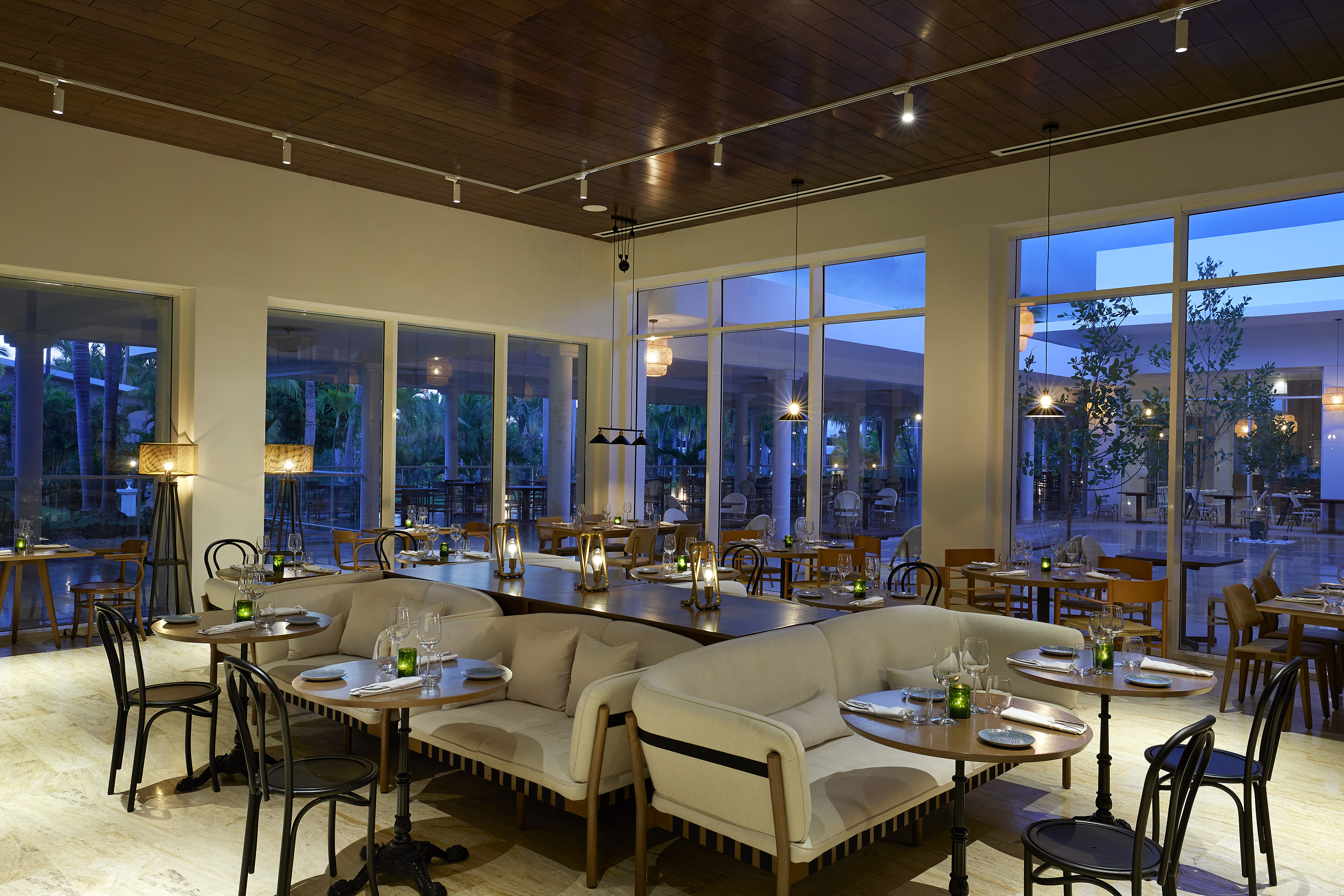 Modern restaurant dining room with plush seating, set tables, and evening views.