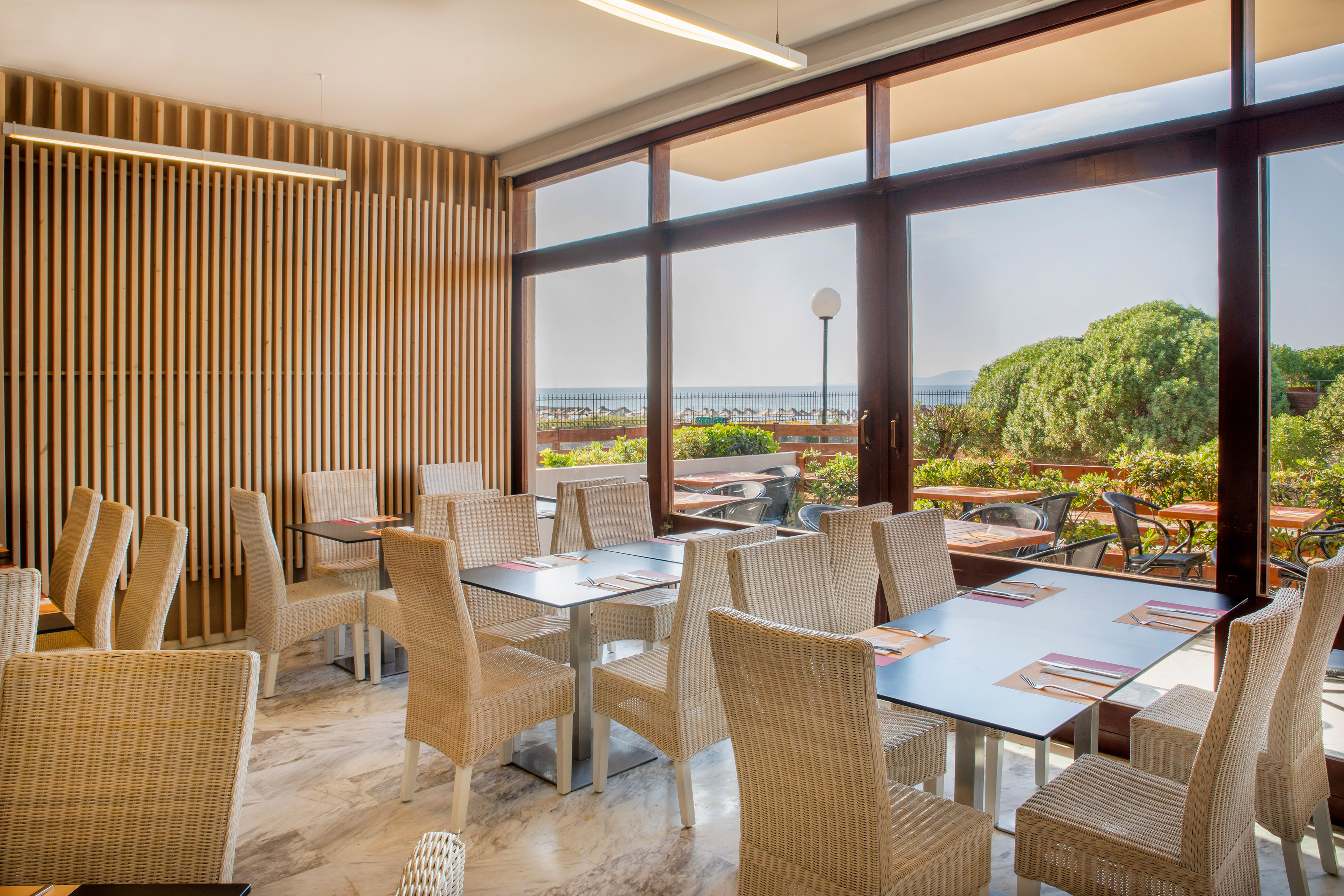 Sunny restaurant with ocean view, wicker chairs, and modern wood paneling.