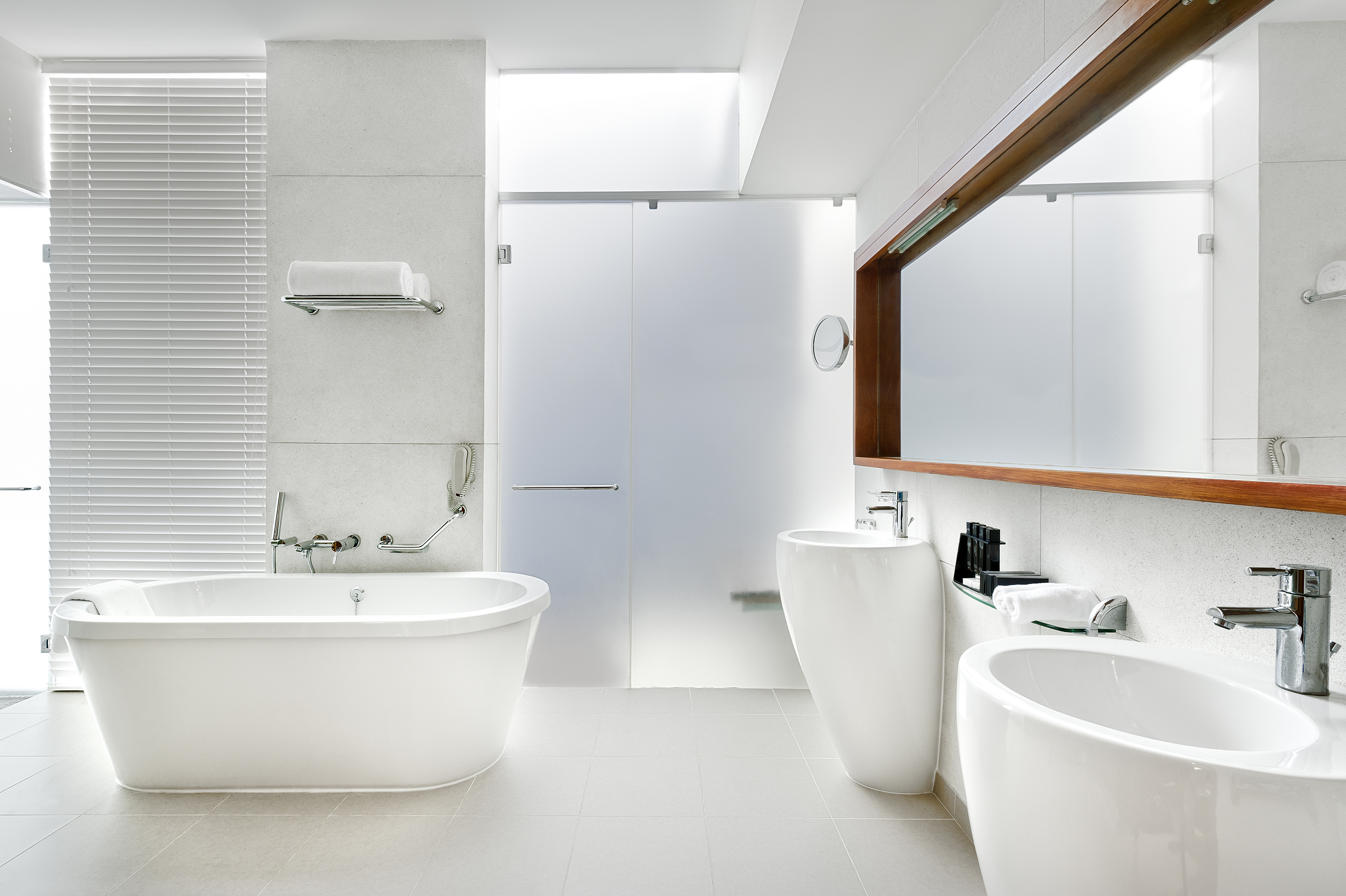 Modern white bathroom with freestanding tub, frosted glass shower, and two sinks.