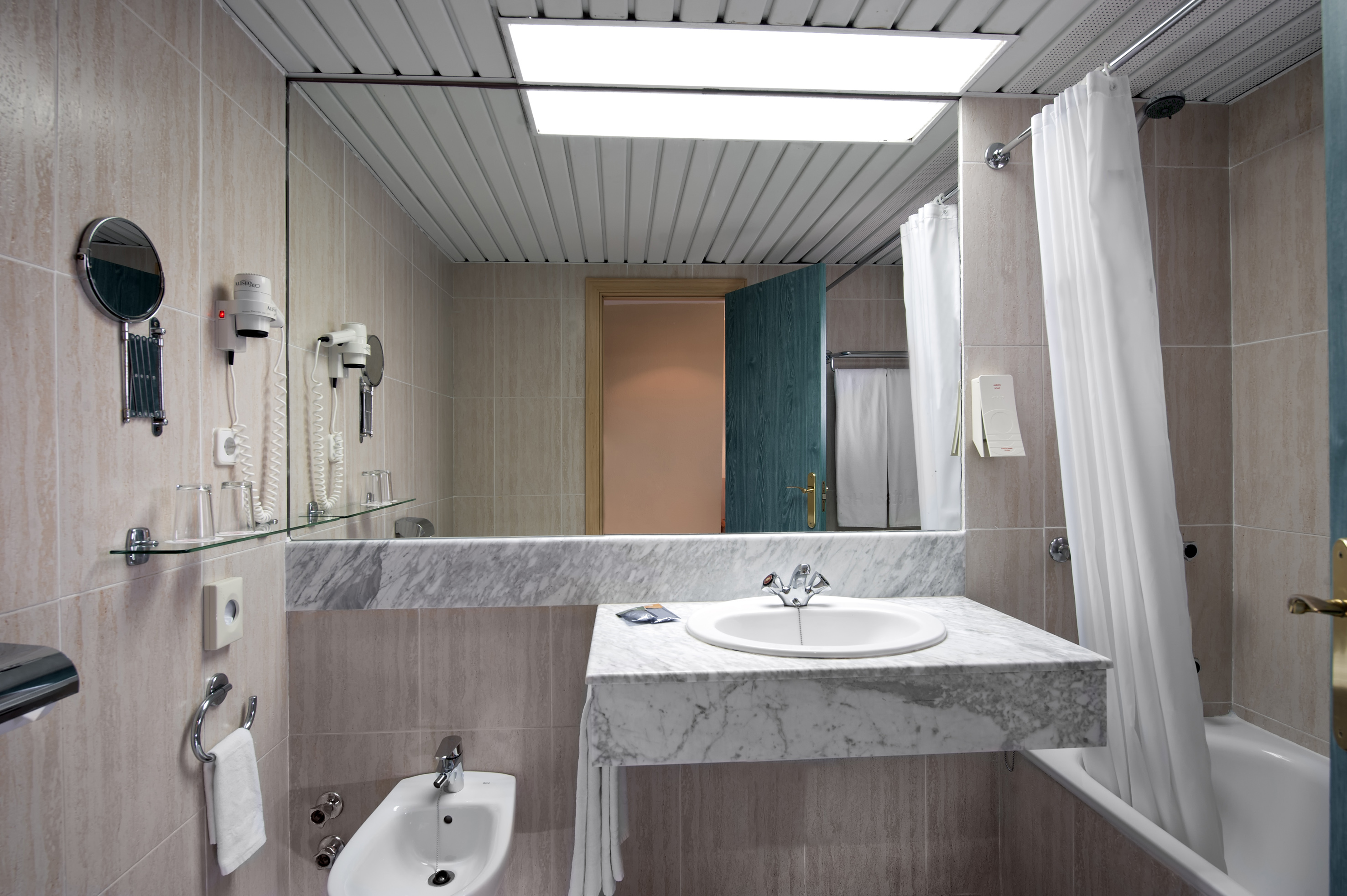 Hotel bathroom with large mirror, marble vanity, sink, bidet, and bathtub.