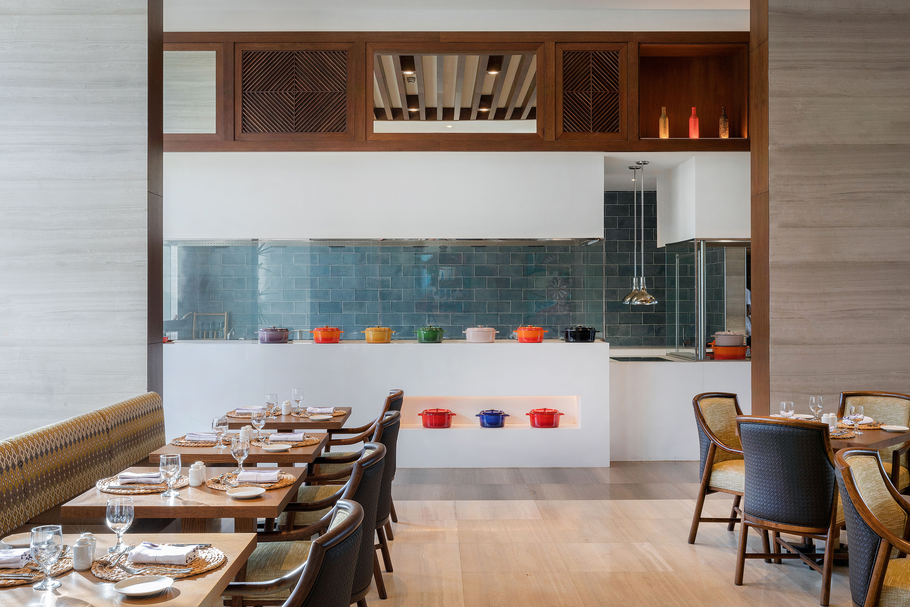 Modern restaurant with open kitchen, teal tiles, colorful pots, and set dining tables.