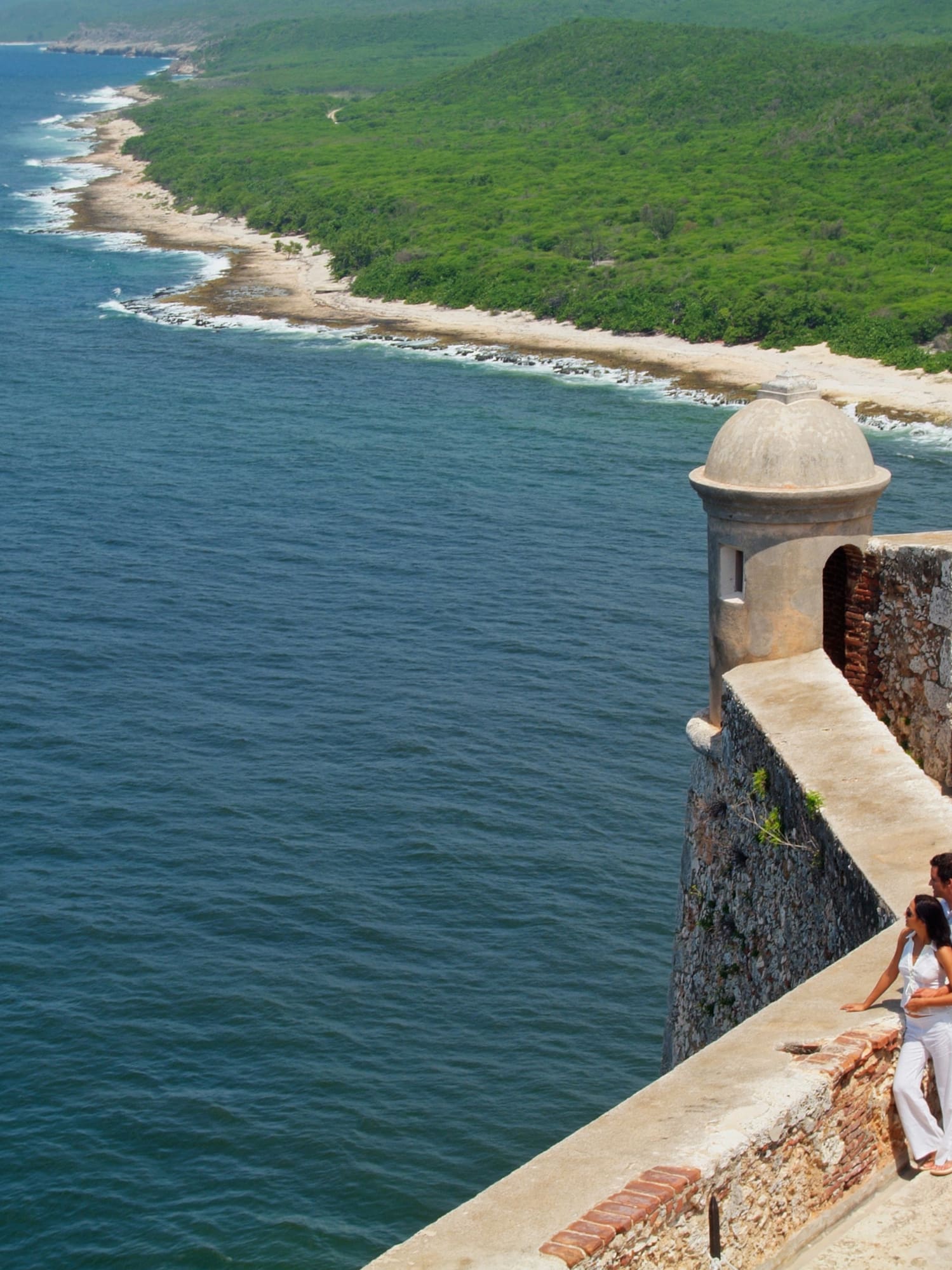 a man and woman standing on a stone wall overlooking a body of water