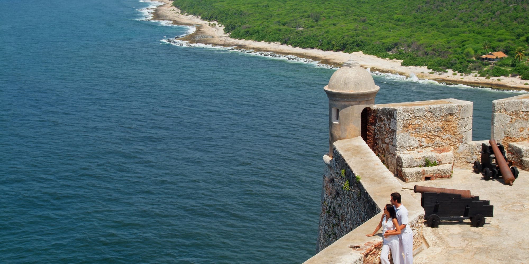 a man and woman standing on a stone wall overlooking a body of water