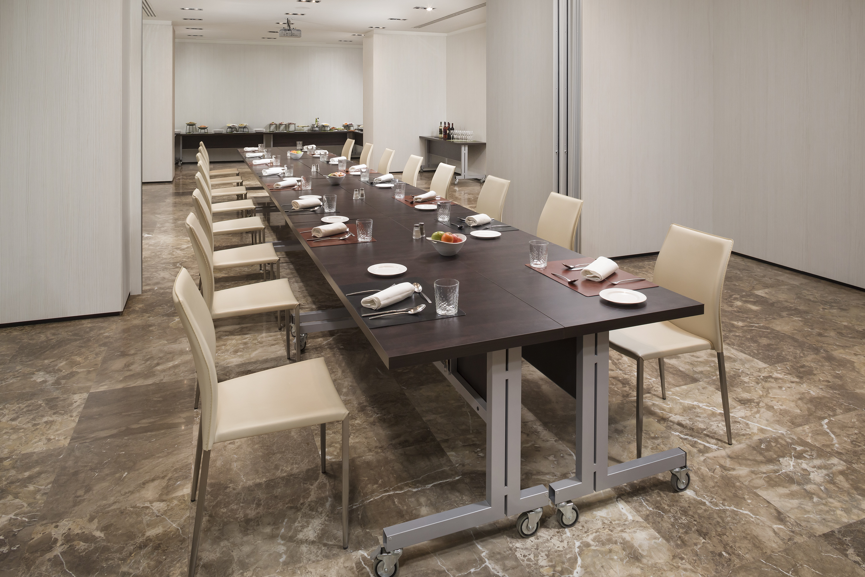 Modern conference room with long table set for event, beige chairs, buffet.