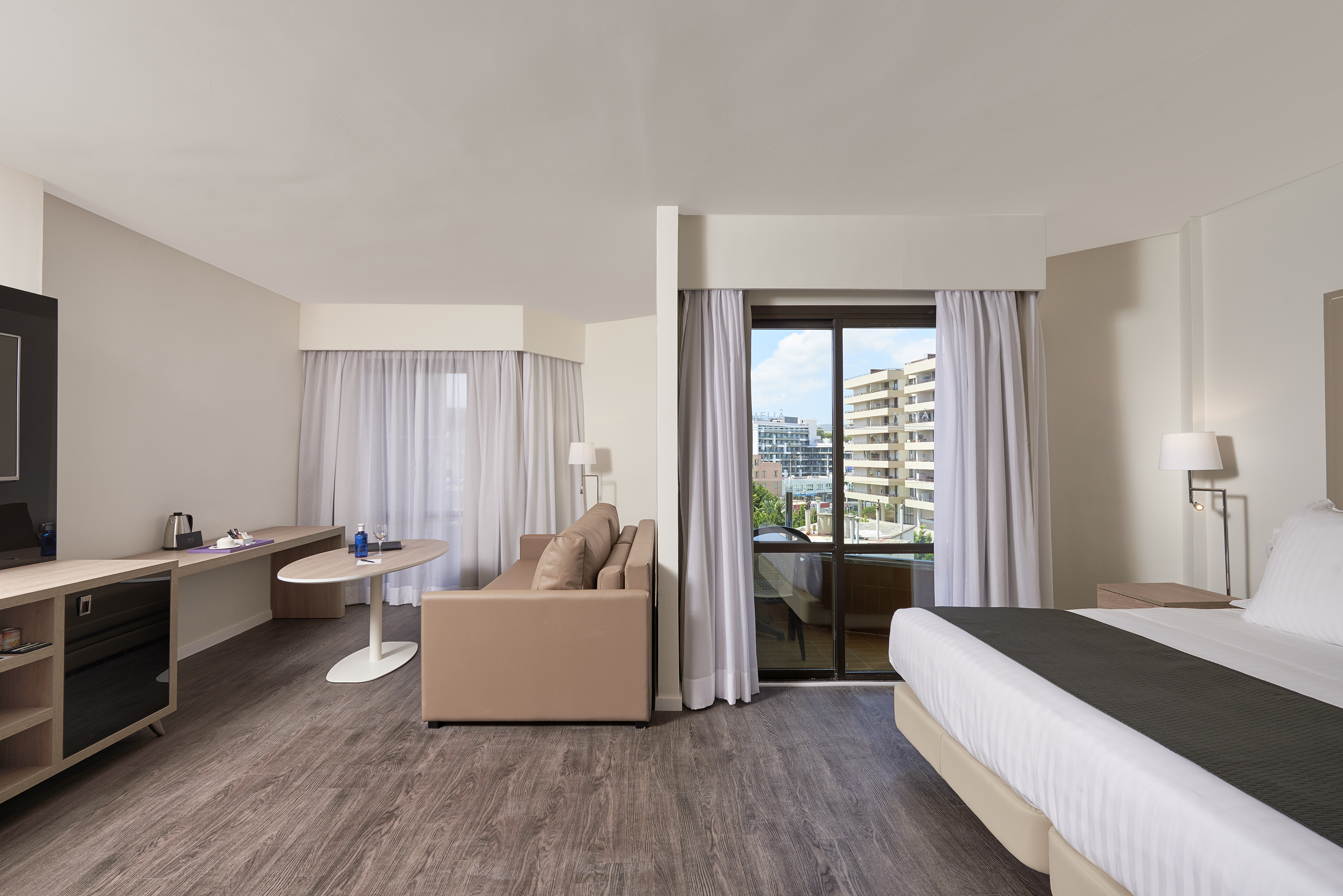 Contemporary hotel suite with bed, sitting area, desk, and city view.