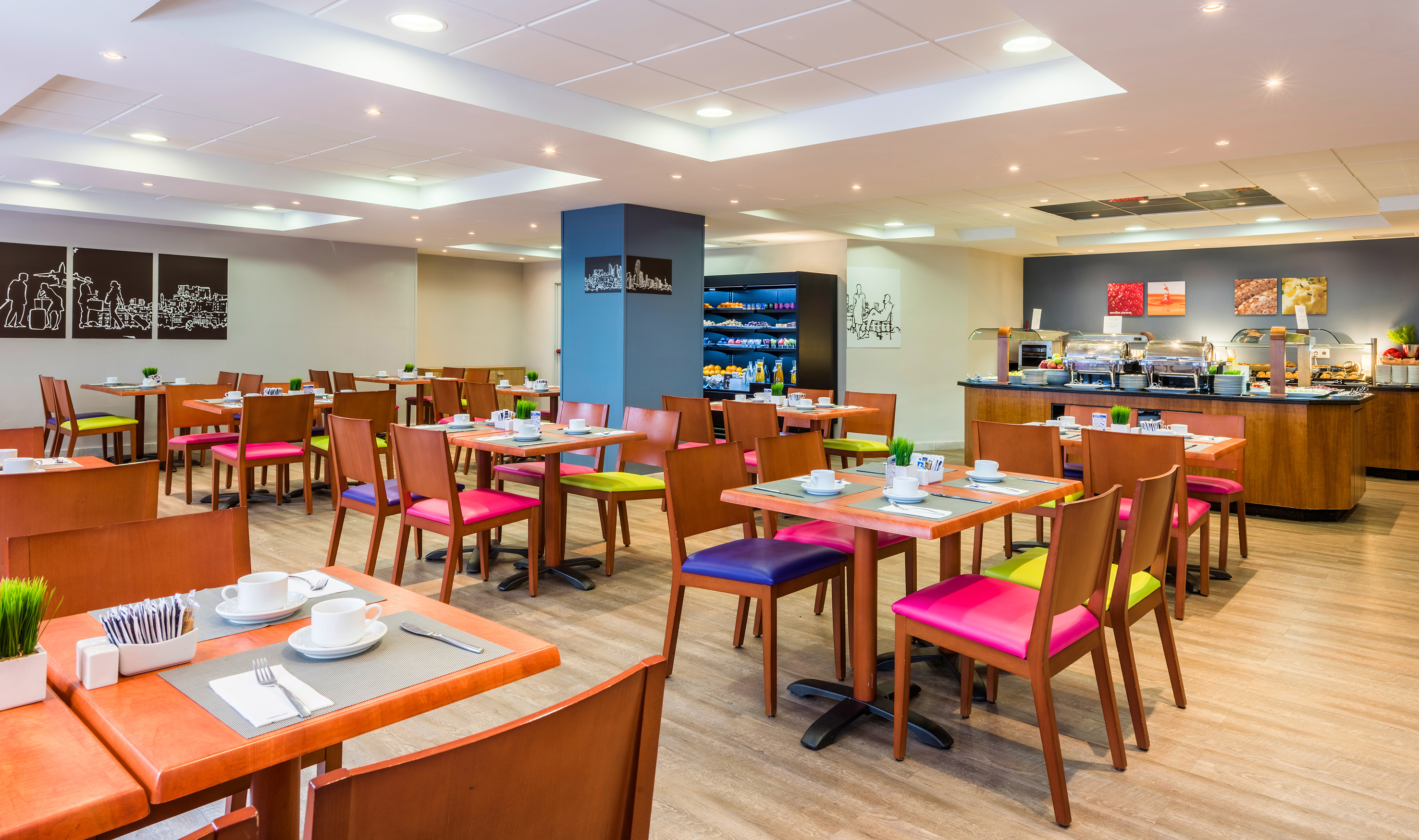 Modern hotel breakfast room with buffet, wooden tables, and colorful chairs.