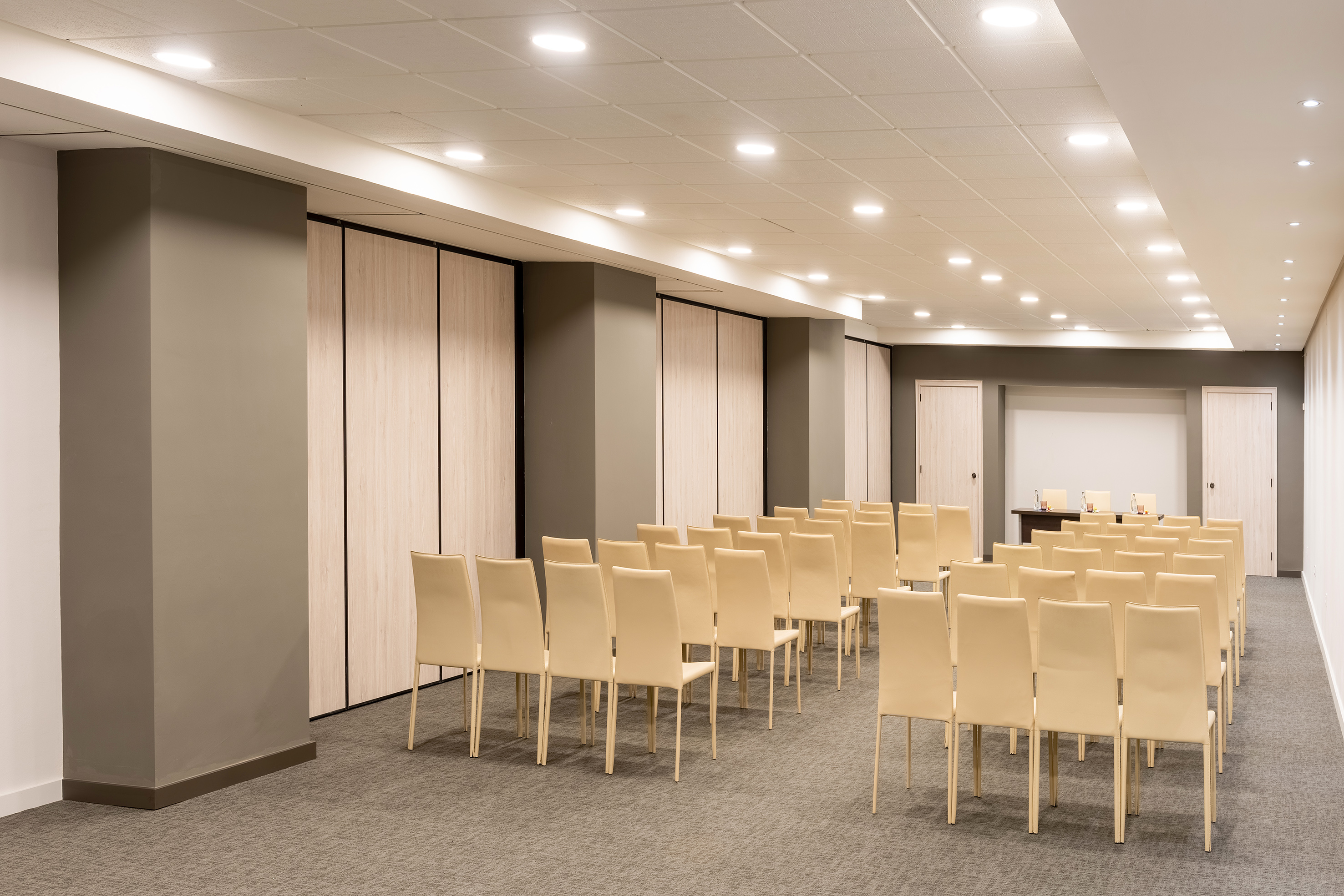 Spacious conference room with rows of beige chairs and ceiling lights.
