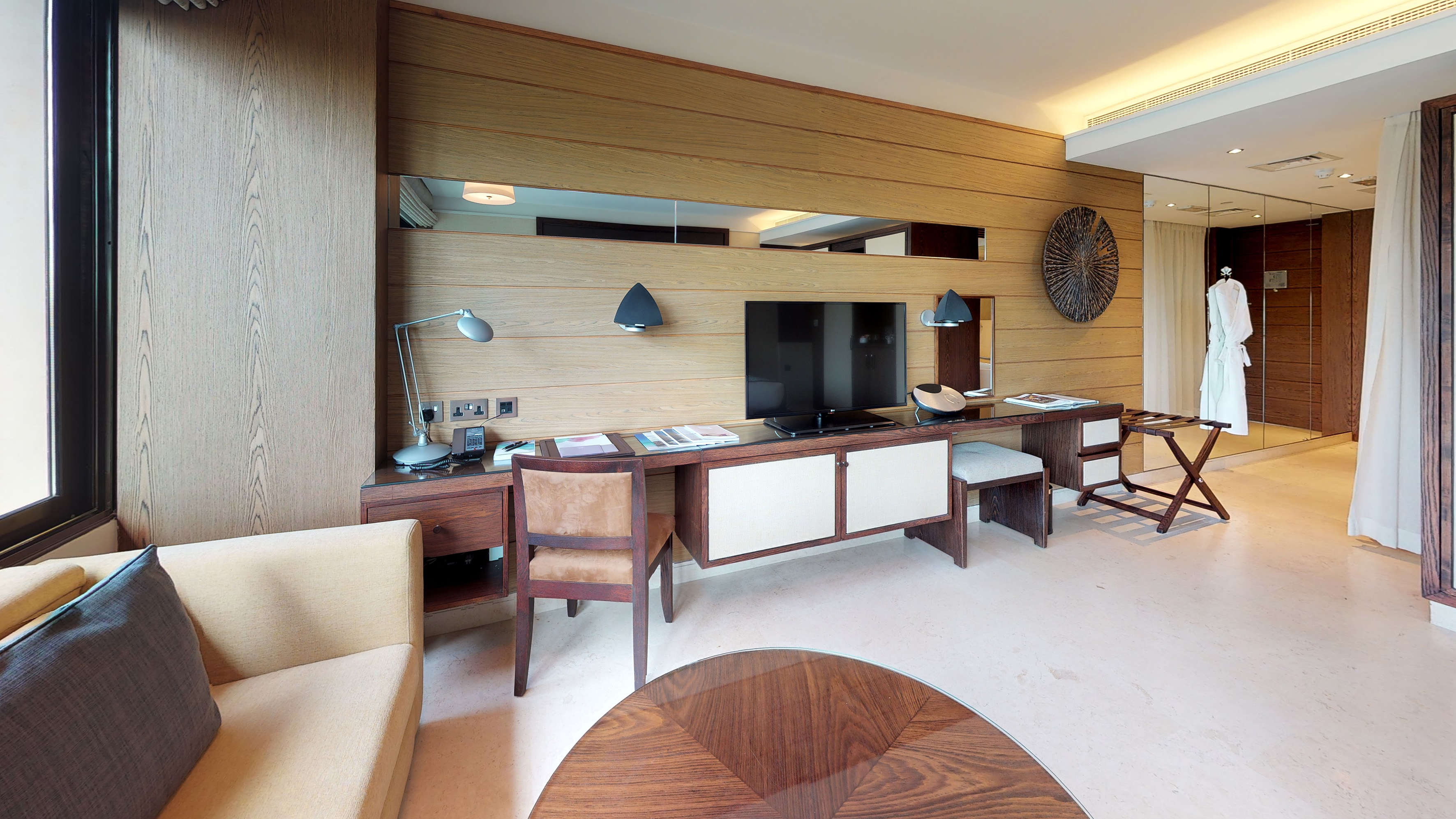 Modern luxury hotel room with wooden wall panels, TV, desk, and sofa.