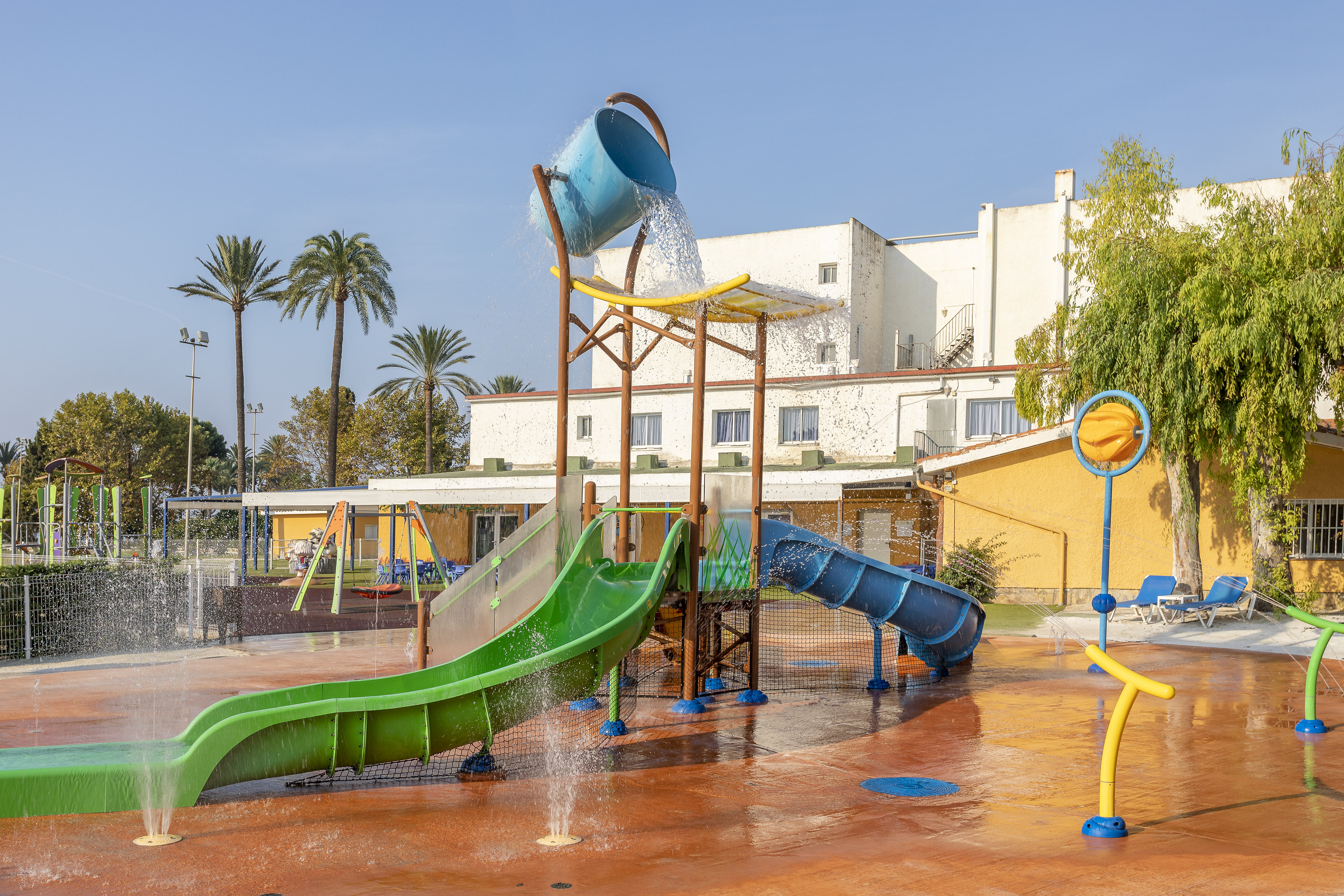 Water park with green and blue slides, tipping bucket, and splash pad at a resort.