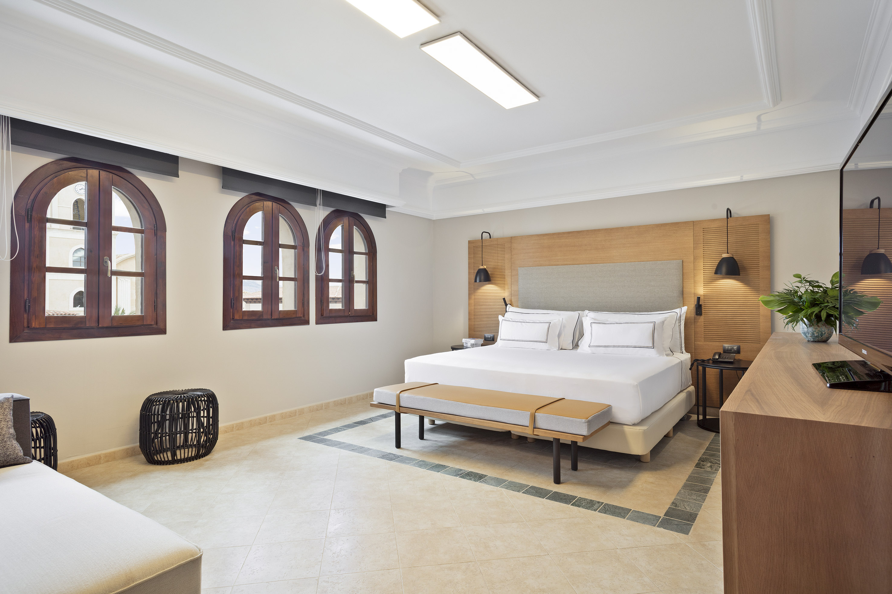 Bright, modern hotel bedroom with king bed, arched windows, and tiled floor.