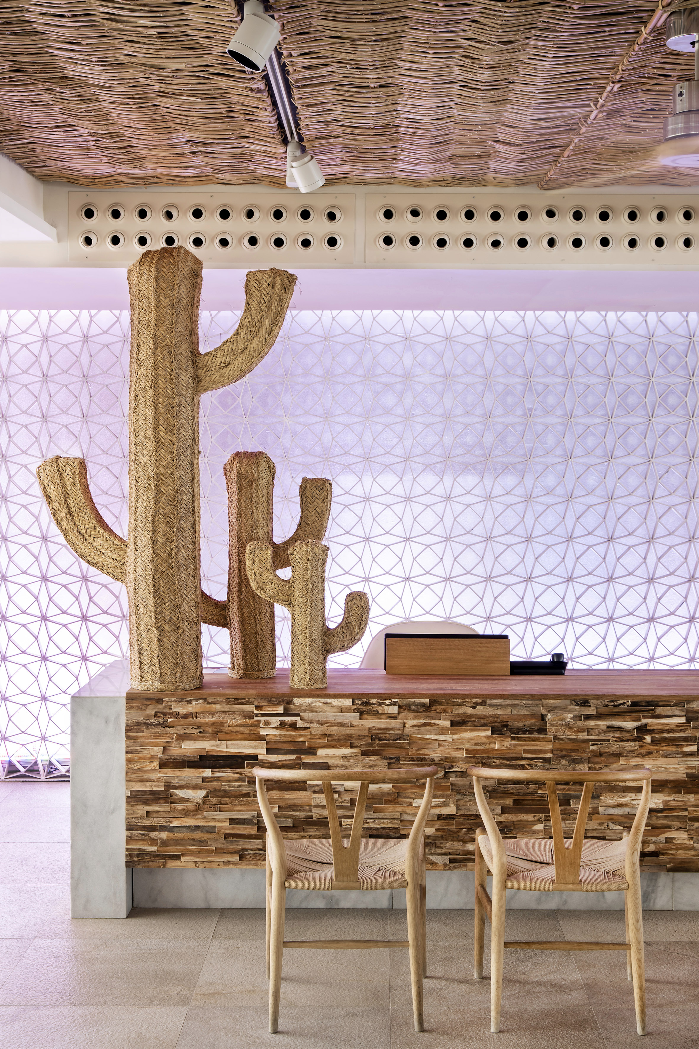 Straw cacti decor on wood reception desk, geometric backlit wall.