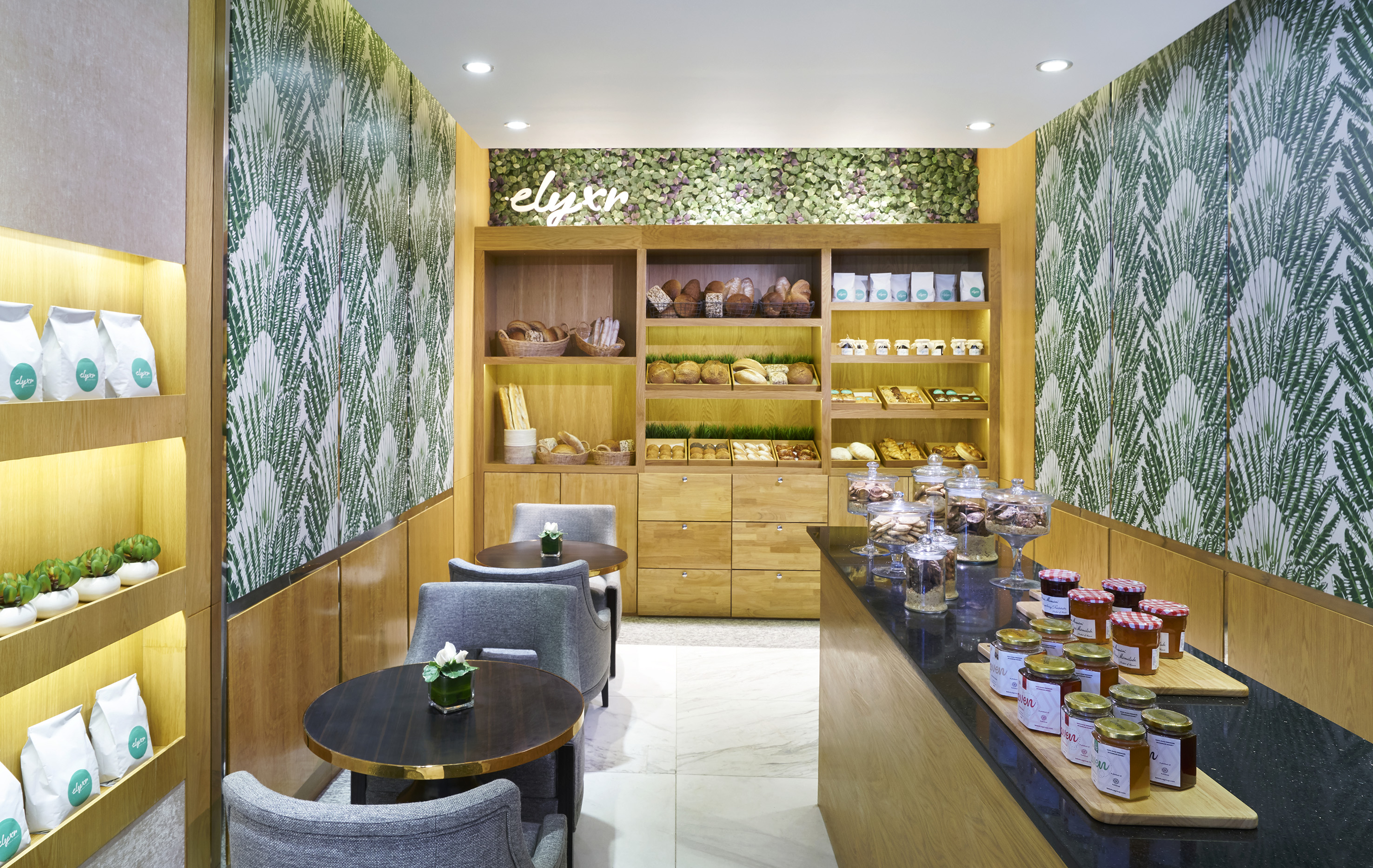 Bakery cafe, wooden shelves of bread, pastries, jams, tropical leaf walls.