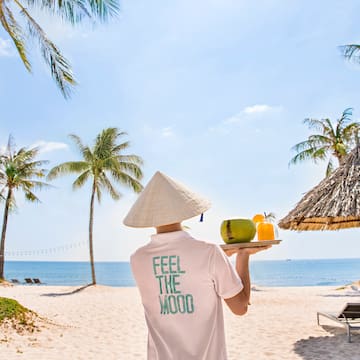 a person wearing a conical hat holding a tray with fruit and a straw umbrella on a beach