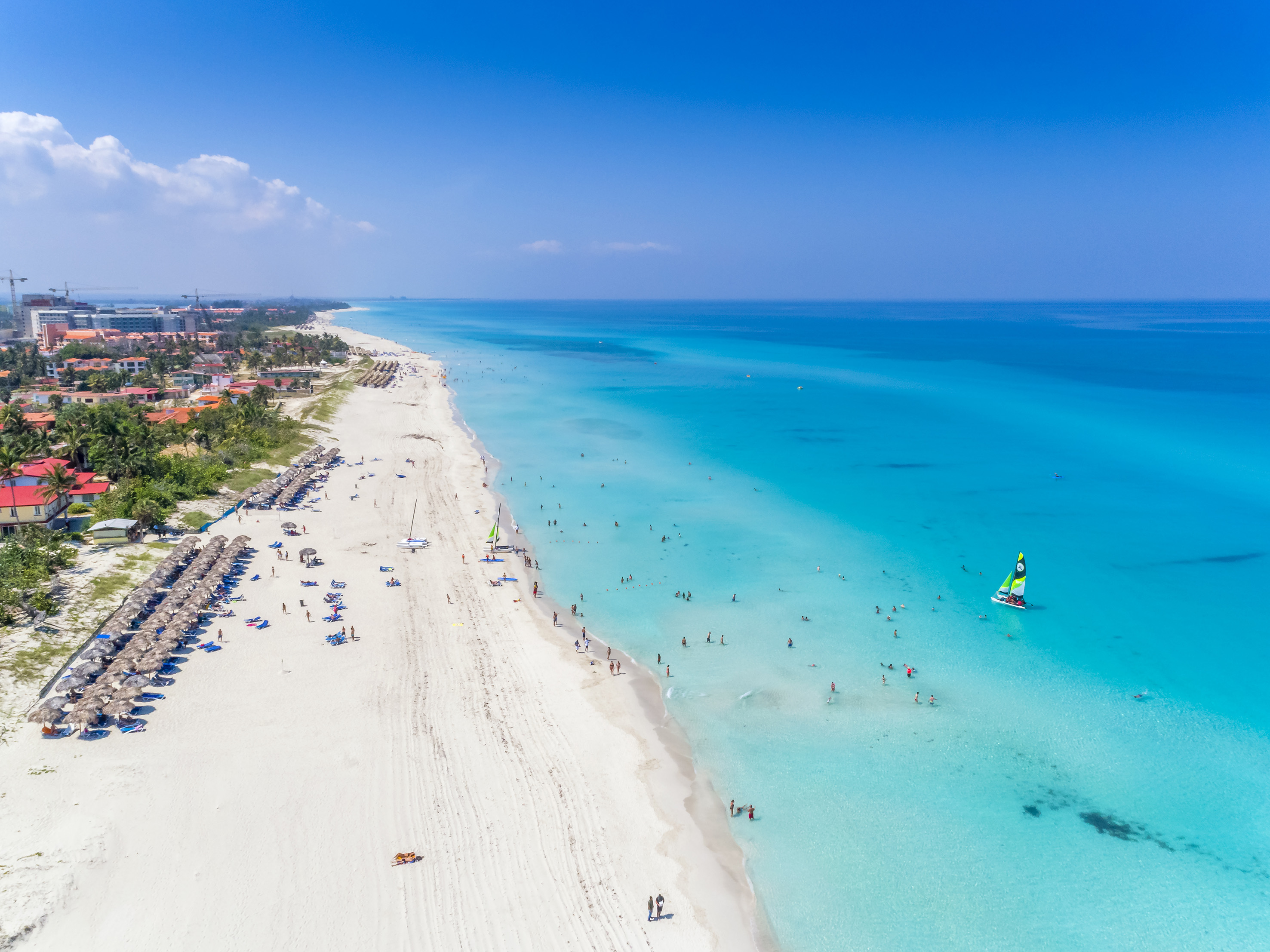 a beach with people and a sailboat