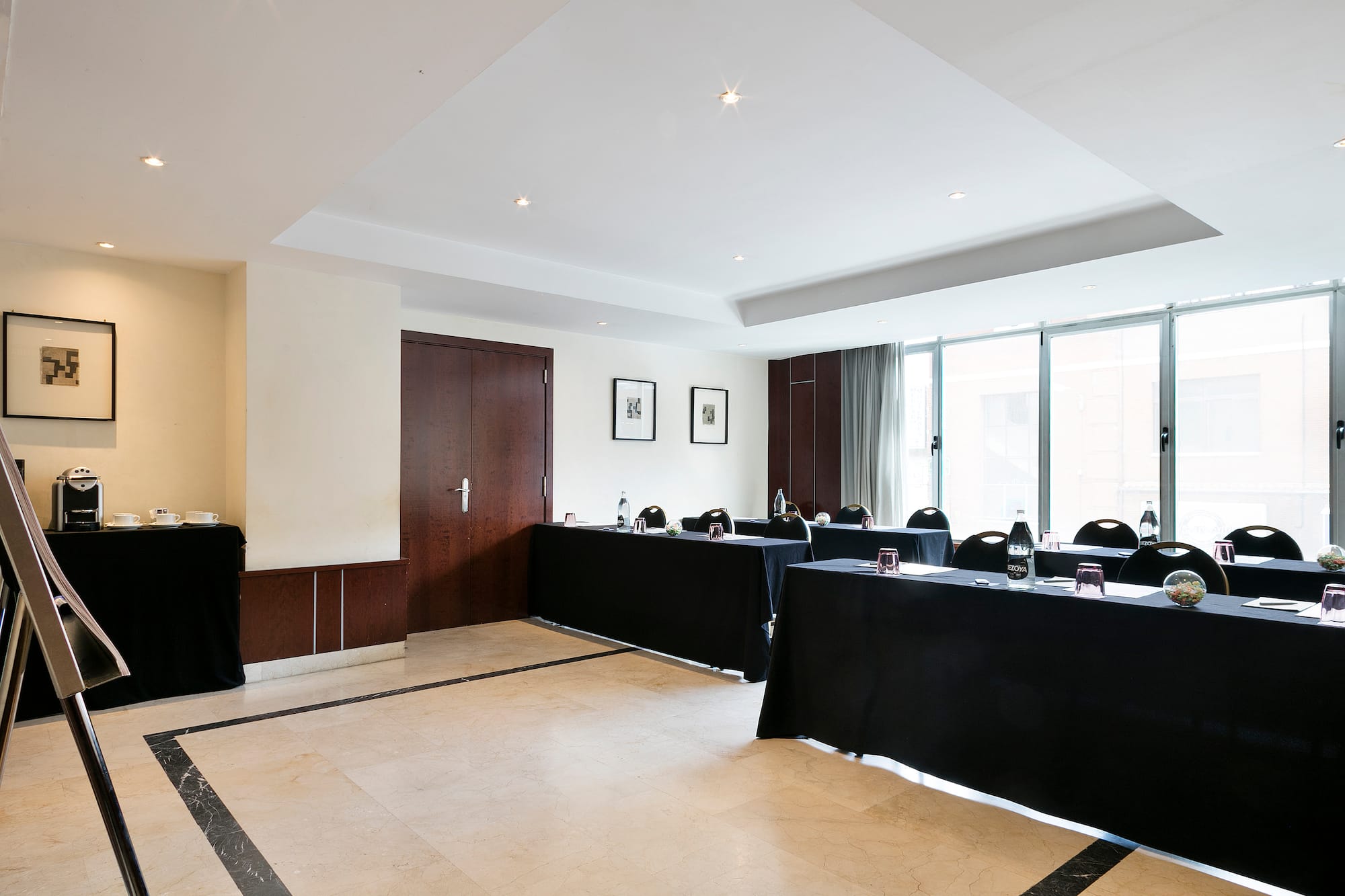 Modern conference room with black tables, chairs, coffee station, and natural light.