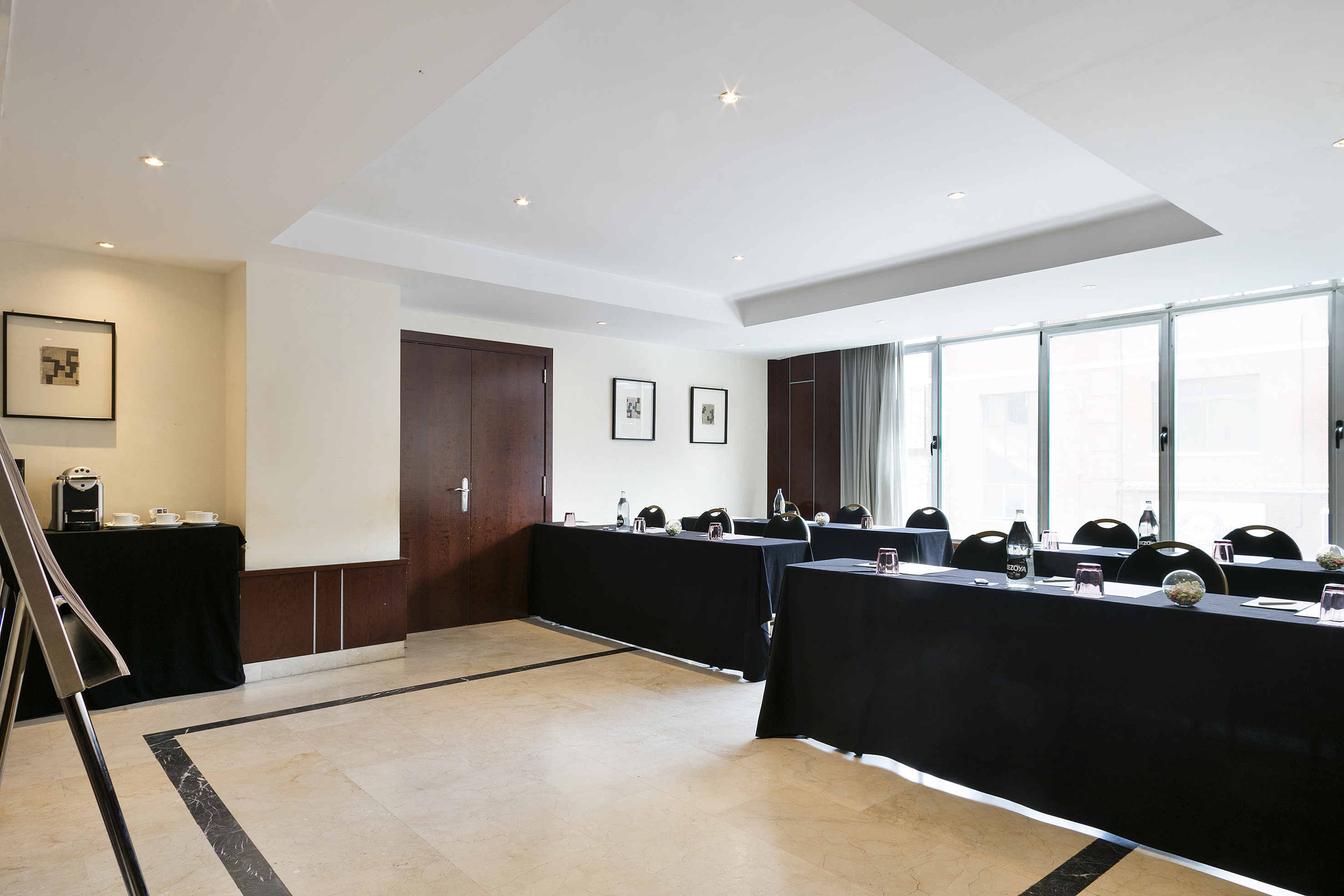 Modern conference room with black tables, chairs, coffee station, and natural light.