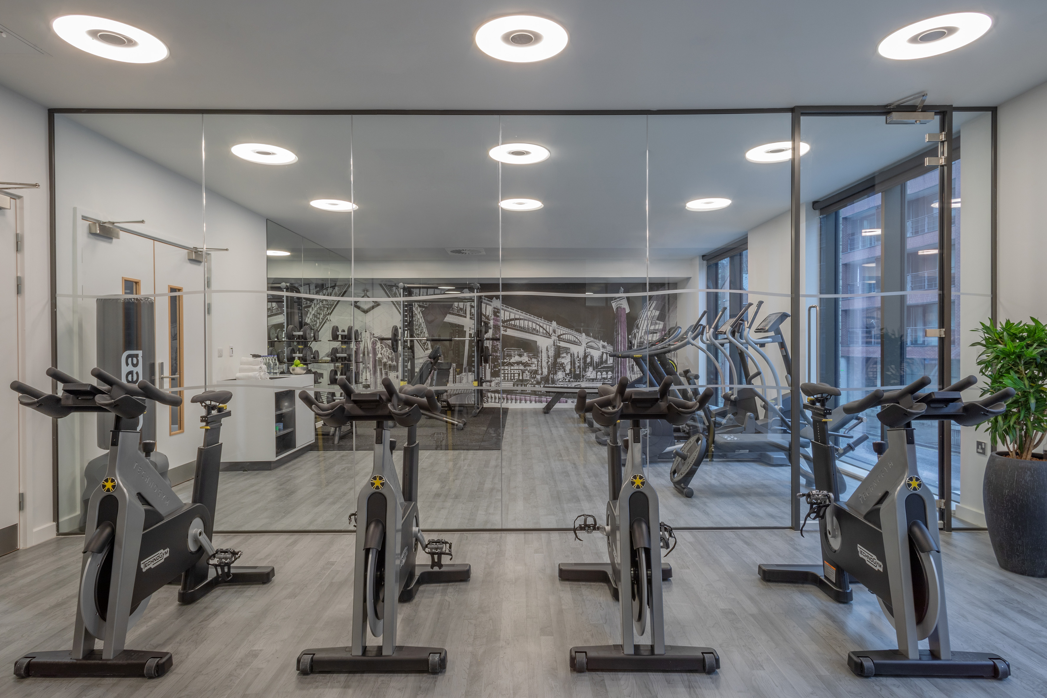Modern gym with spin bikes, mirrored wall, and reflections of fitness equipment.