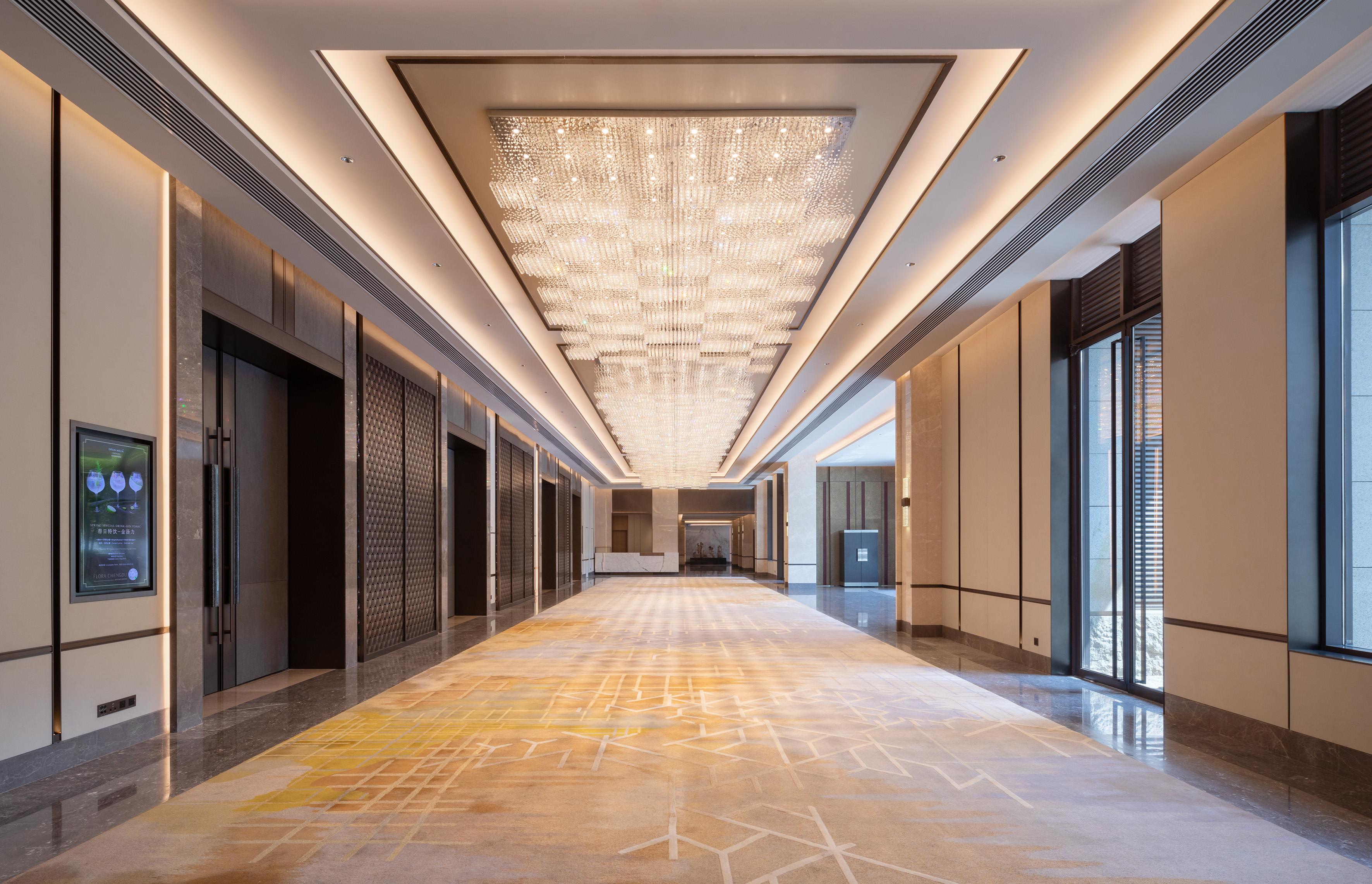 Elegant modern hallway with grand crystal chandelier and patterned carpet.