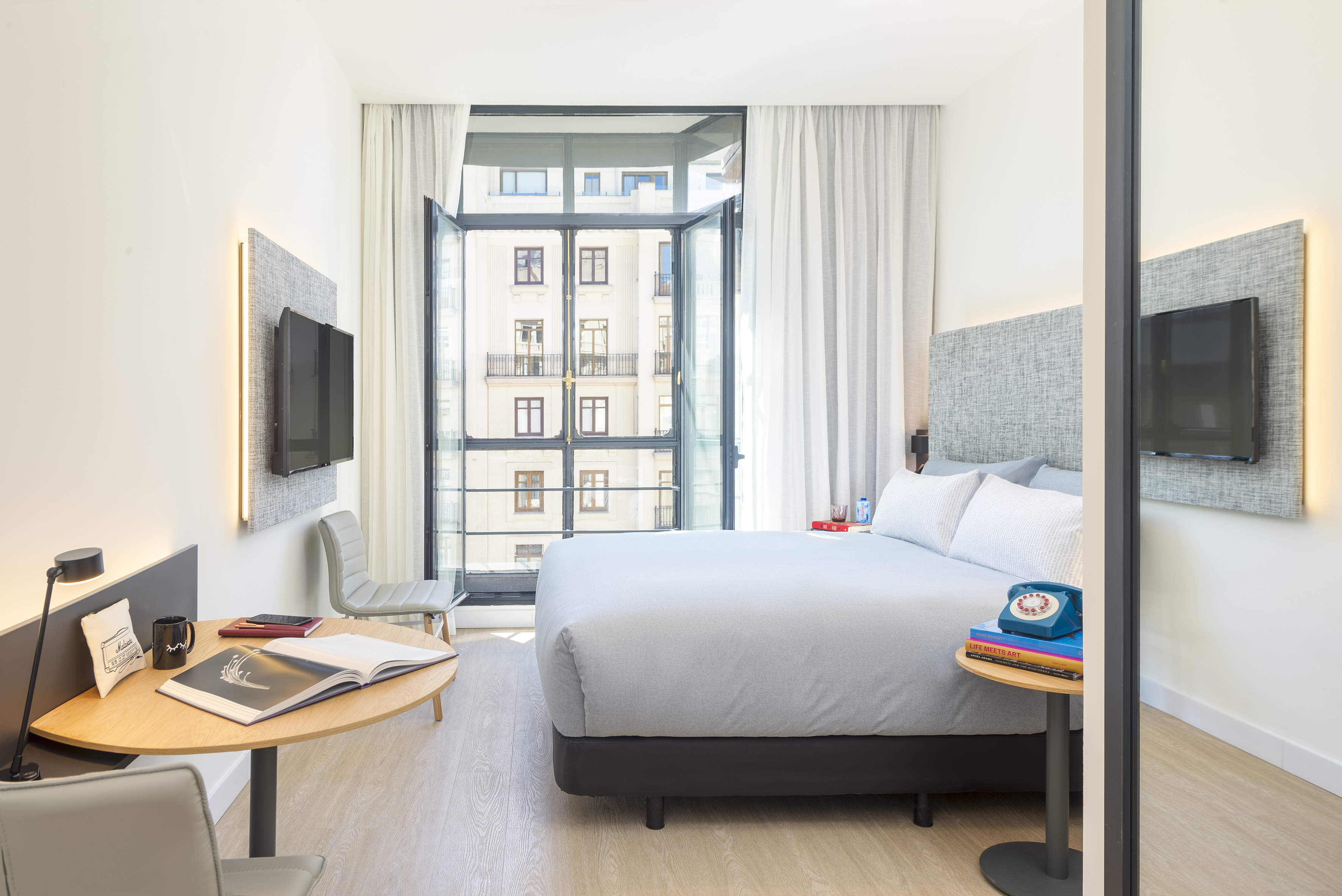 Stylish hotel bedroom with grey bed, workspace, and city view balcony.