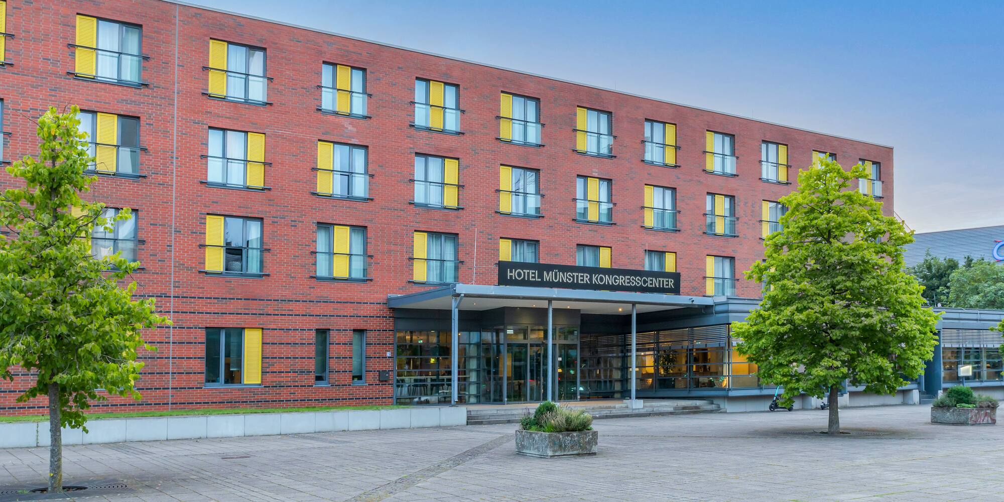 Hotel Münster Kongresscenter: red brick building, yellow shutters, paved entrance.