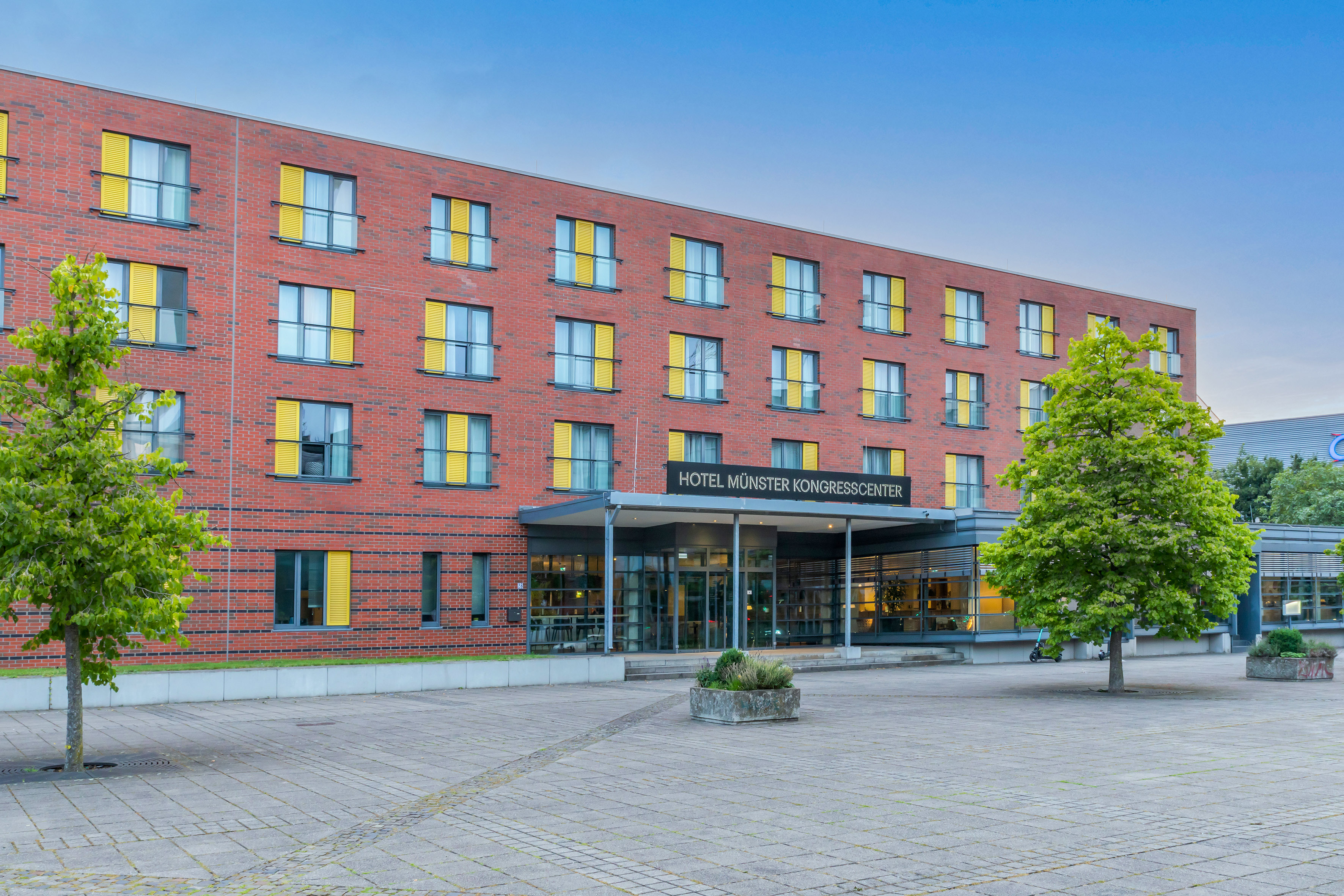 Hotel Münster Kongresscenter: red brick building, yellow shutters, paved entrance.