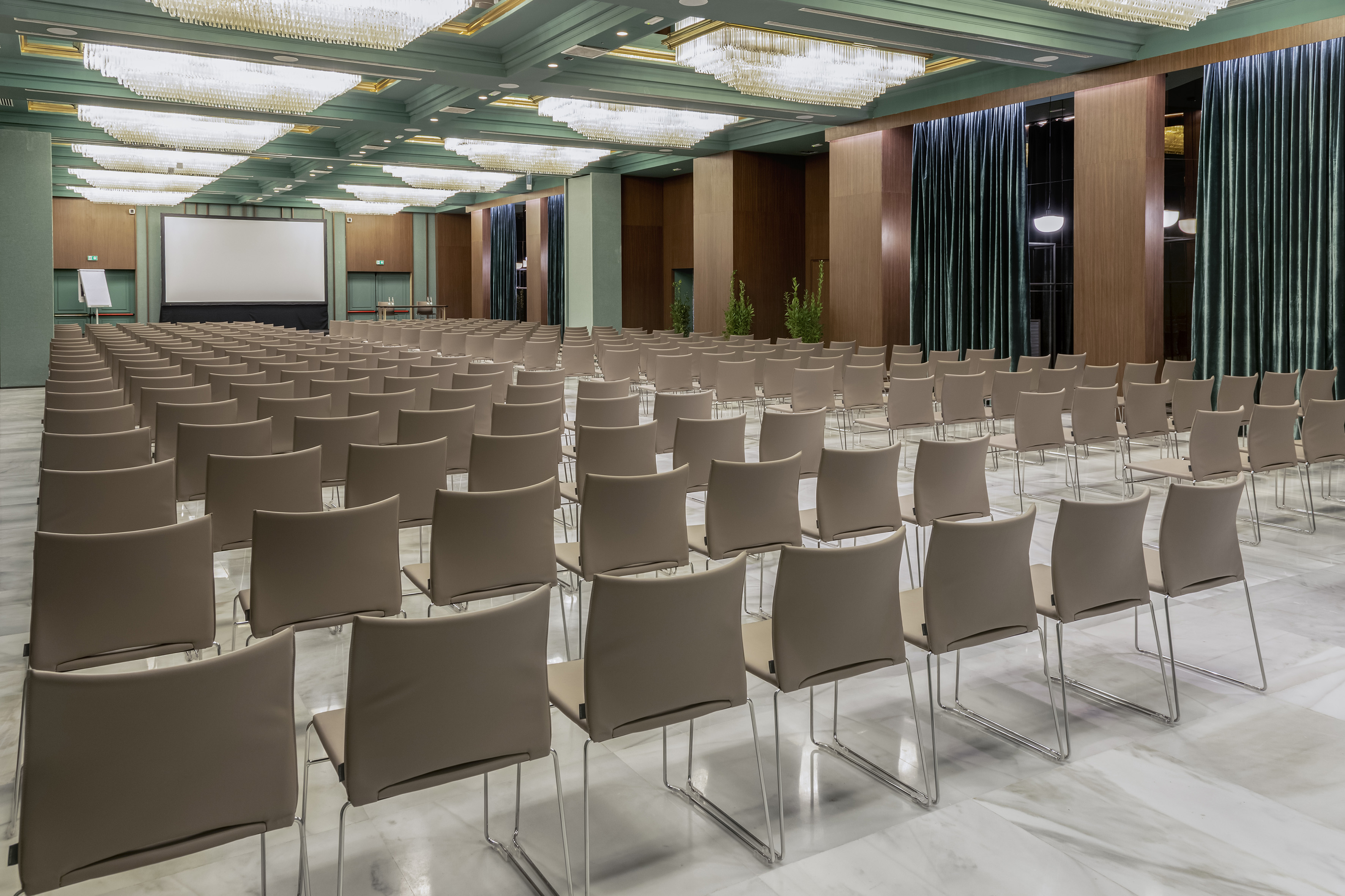 Empty conference room with rows of chairs, projector screen, elegant chandeliers.