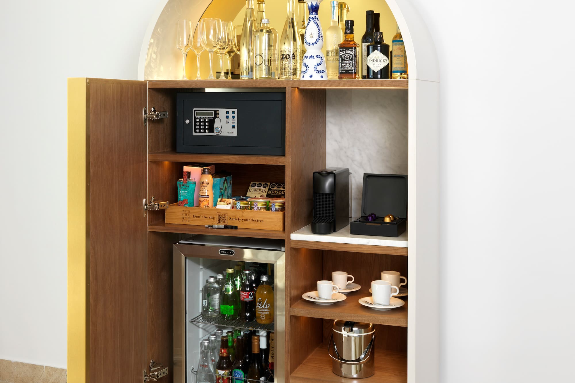 Minibar de hotel moderno con bebidas variadas, máquina de café y caja fuerte.