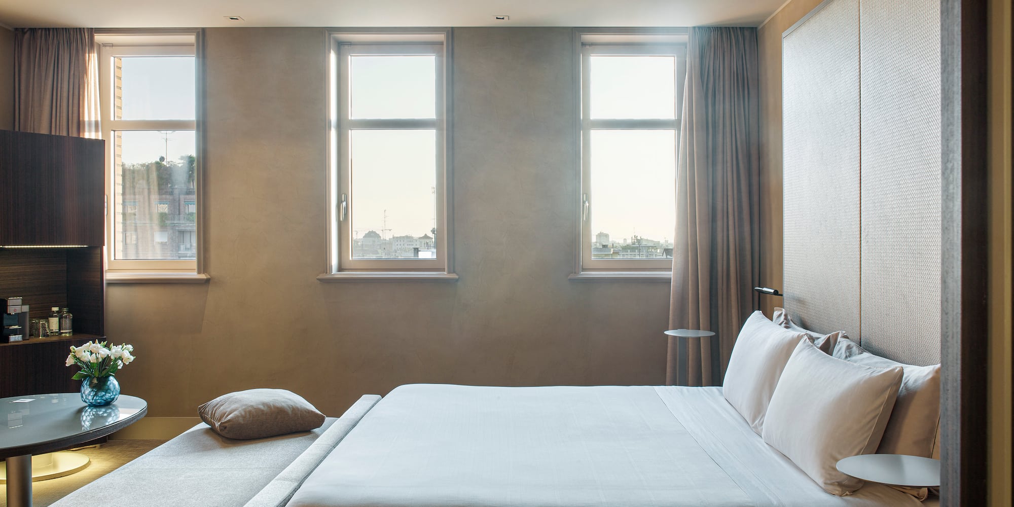 a bed with pillows and a table in a room with windows