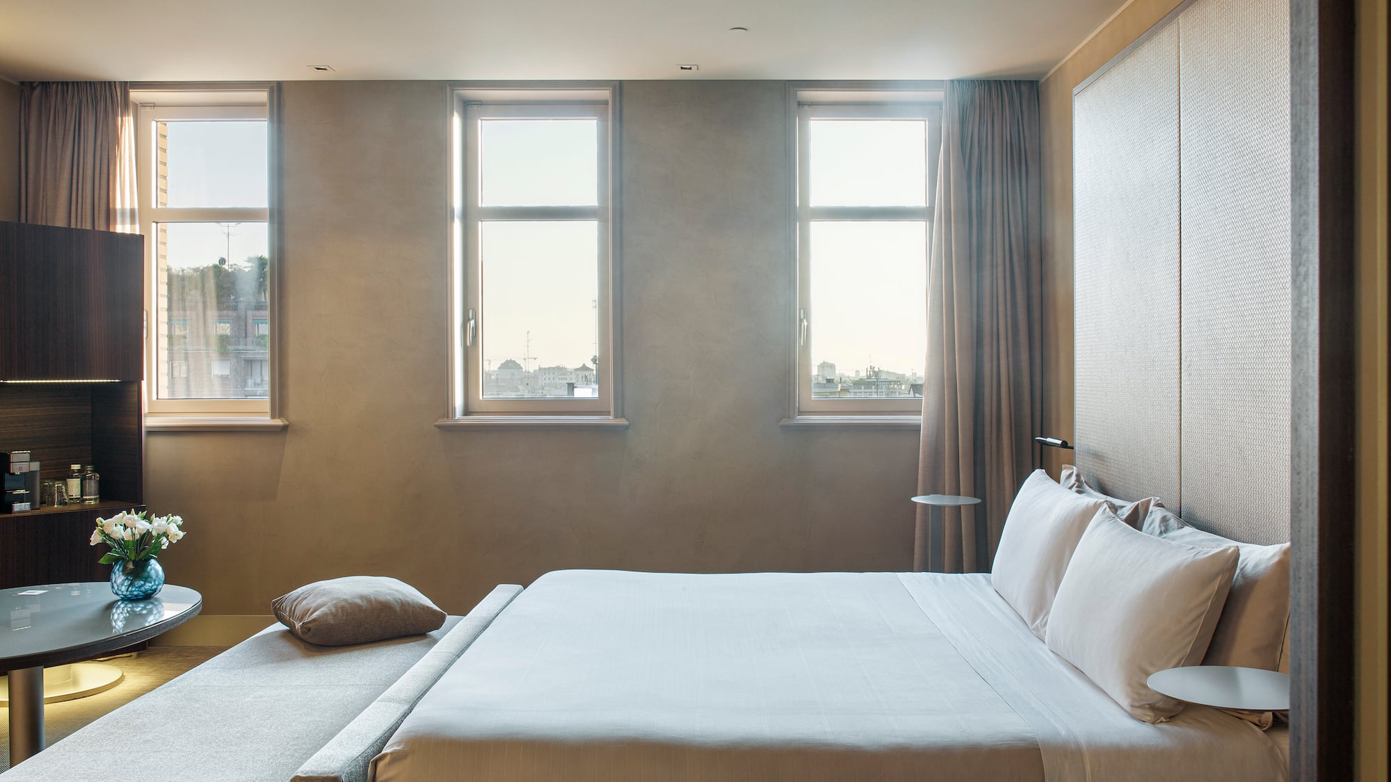 a bed with pillows and a table in a room with windows