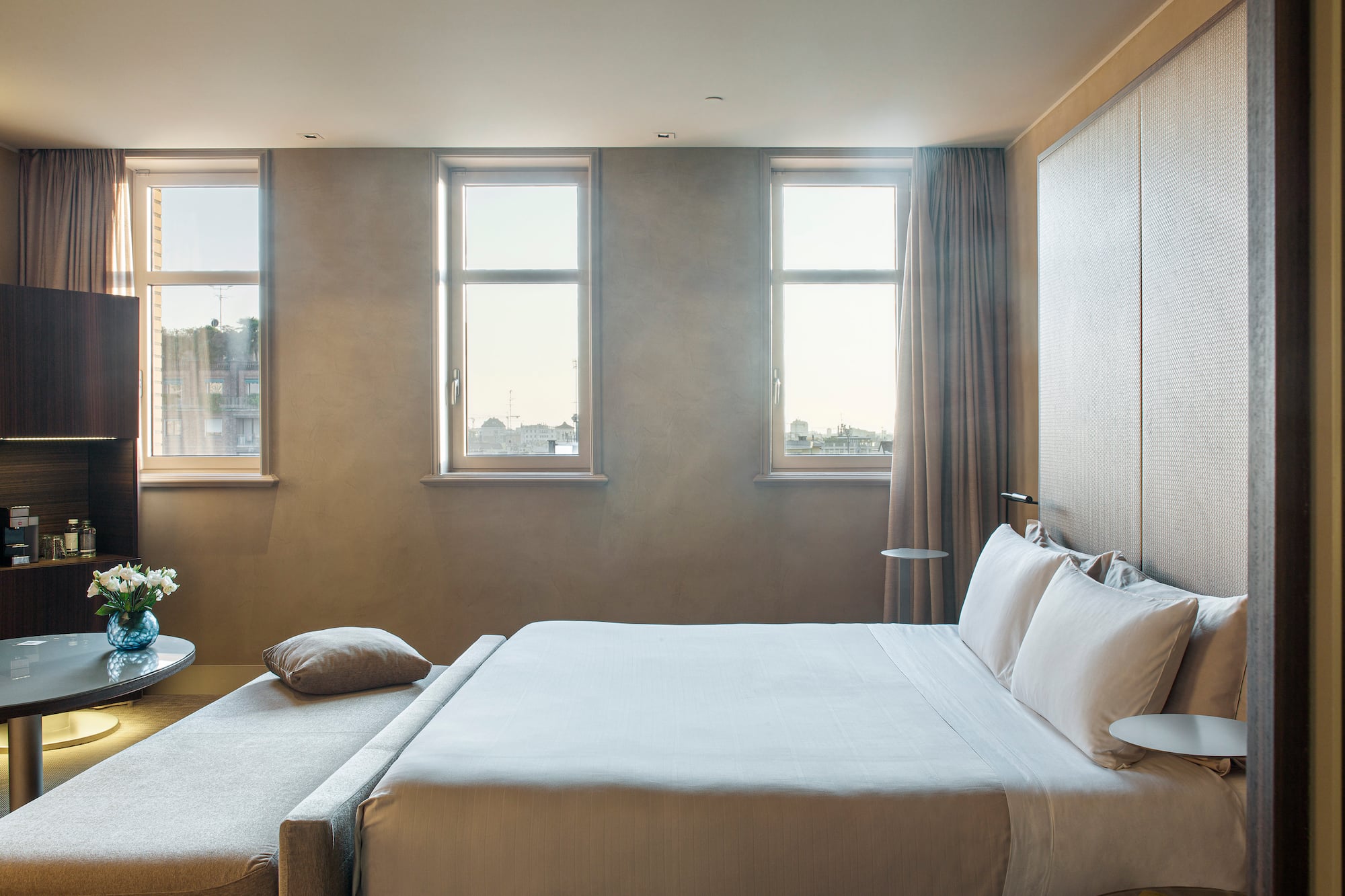 a bed with pillows and a table in a room with windows