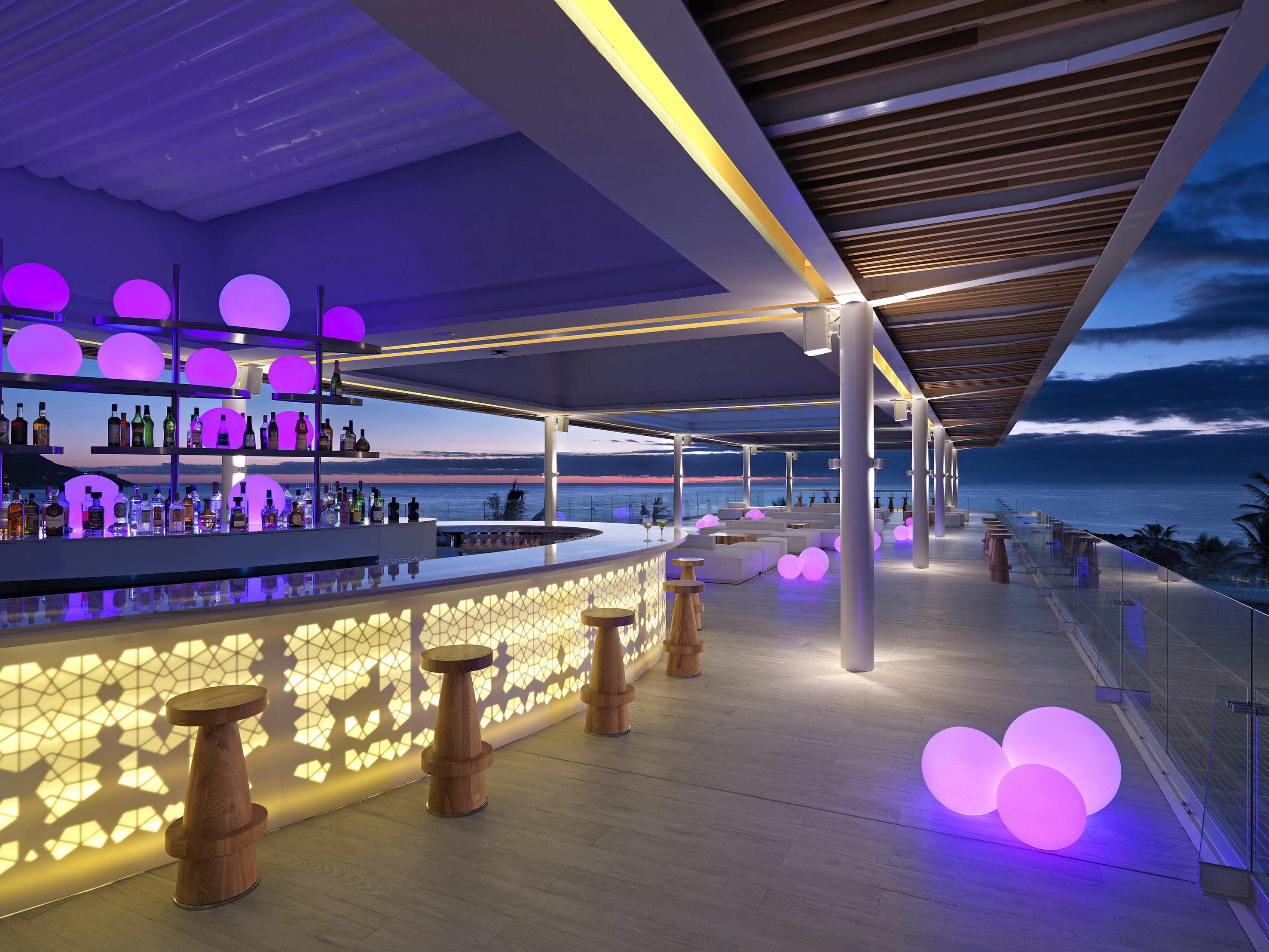 Rooftop ocean view bar at dusk with purple glowing lights and modern illuminated counter.