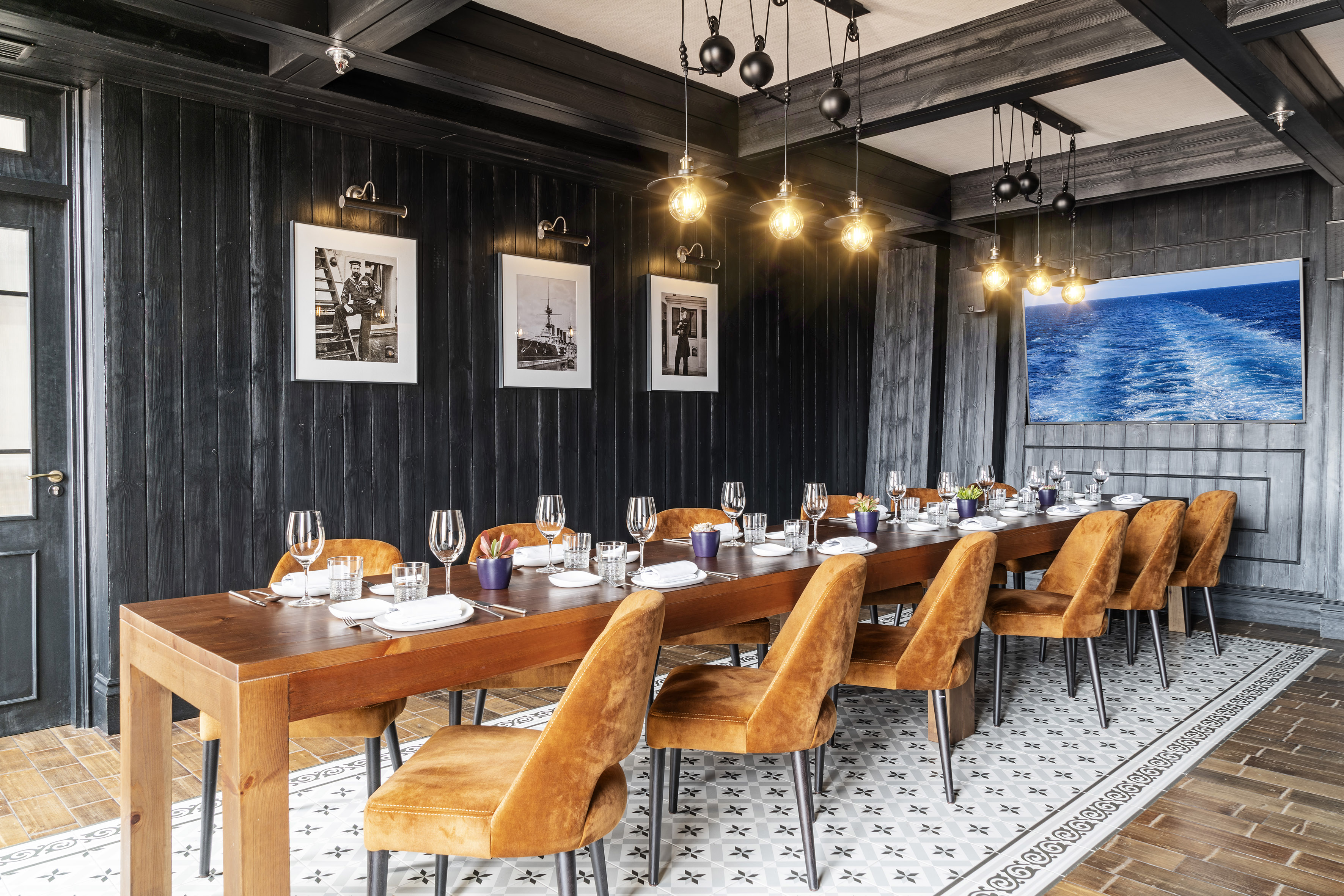 Long dining table with amber chairs in a dark wood room, nautical decor.