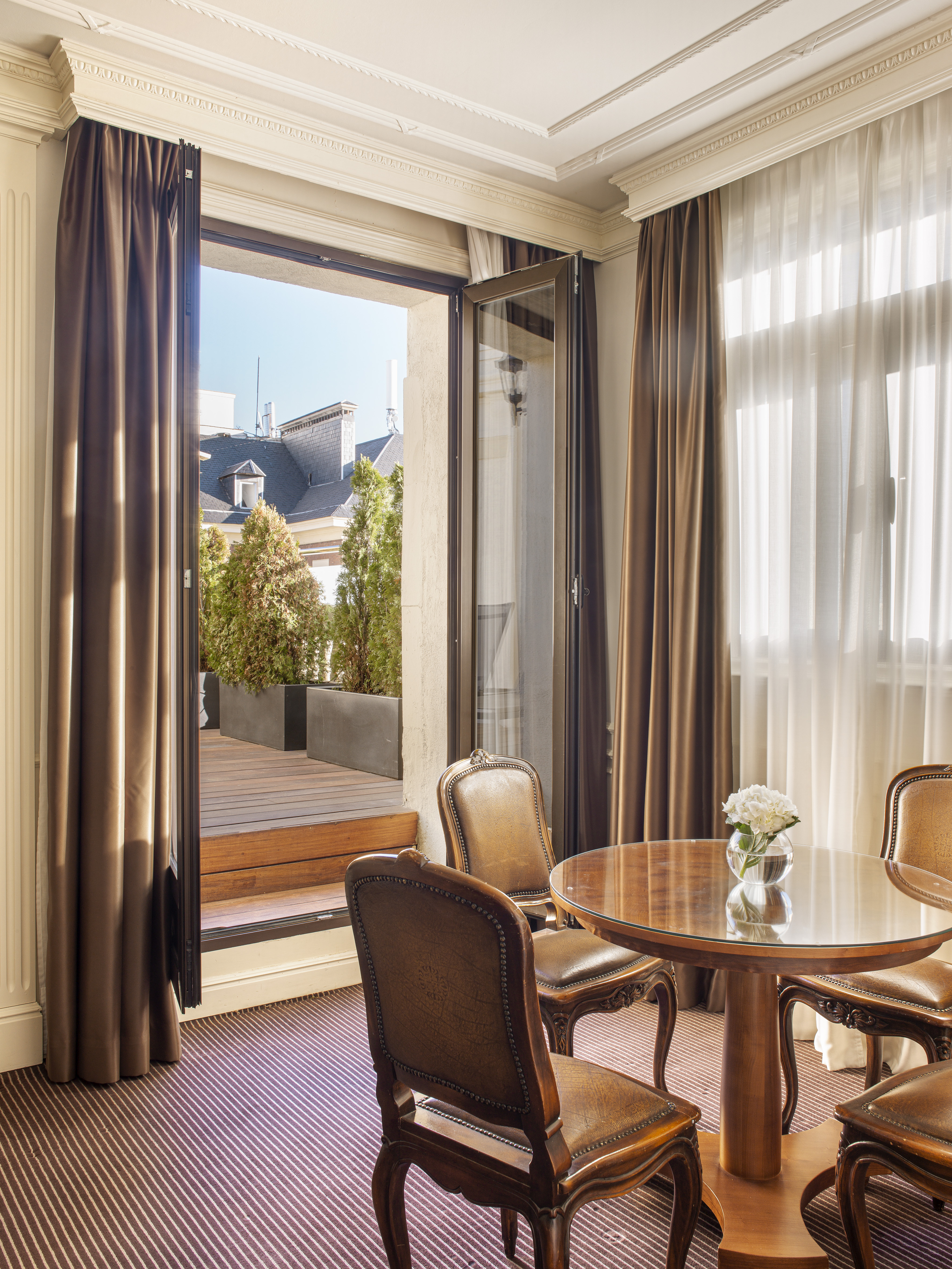 Classic hotel room with dining area, open balcony, and cityscape.