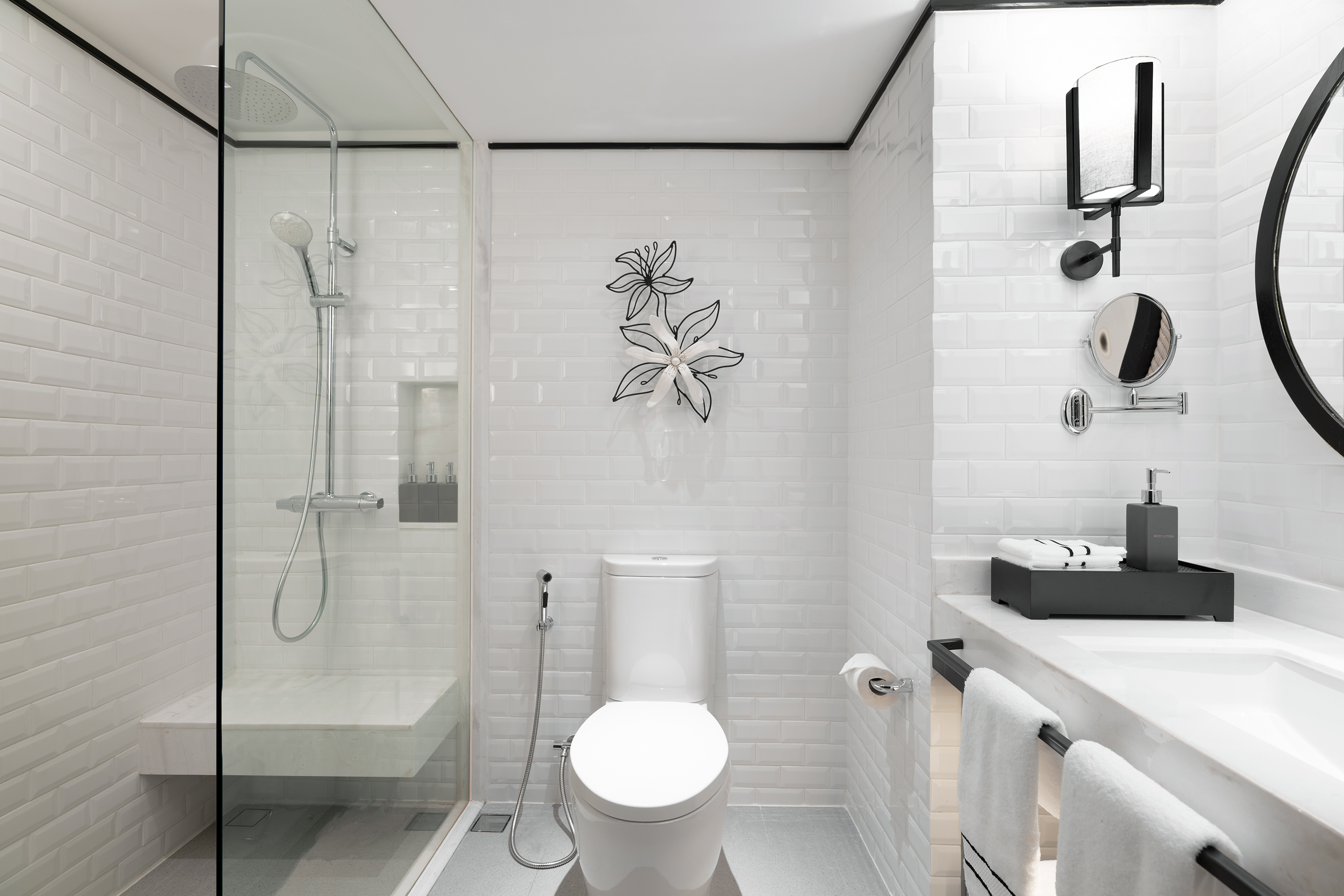 Modern white bathroom with walk-in shower, toilet, vanity, and black decor.