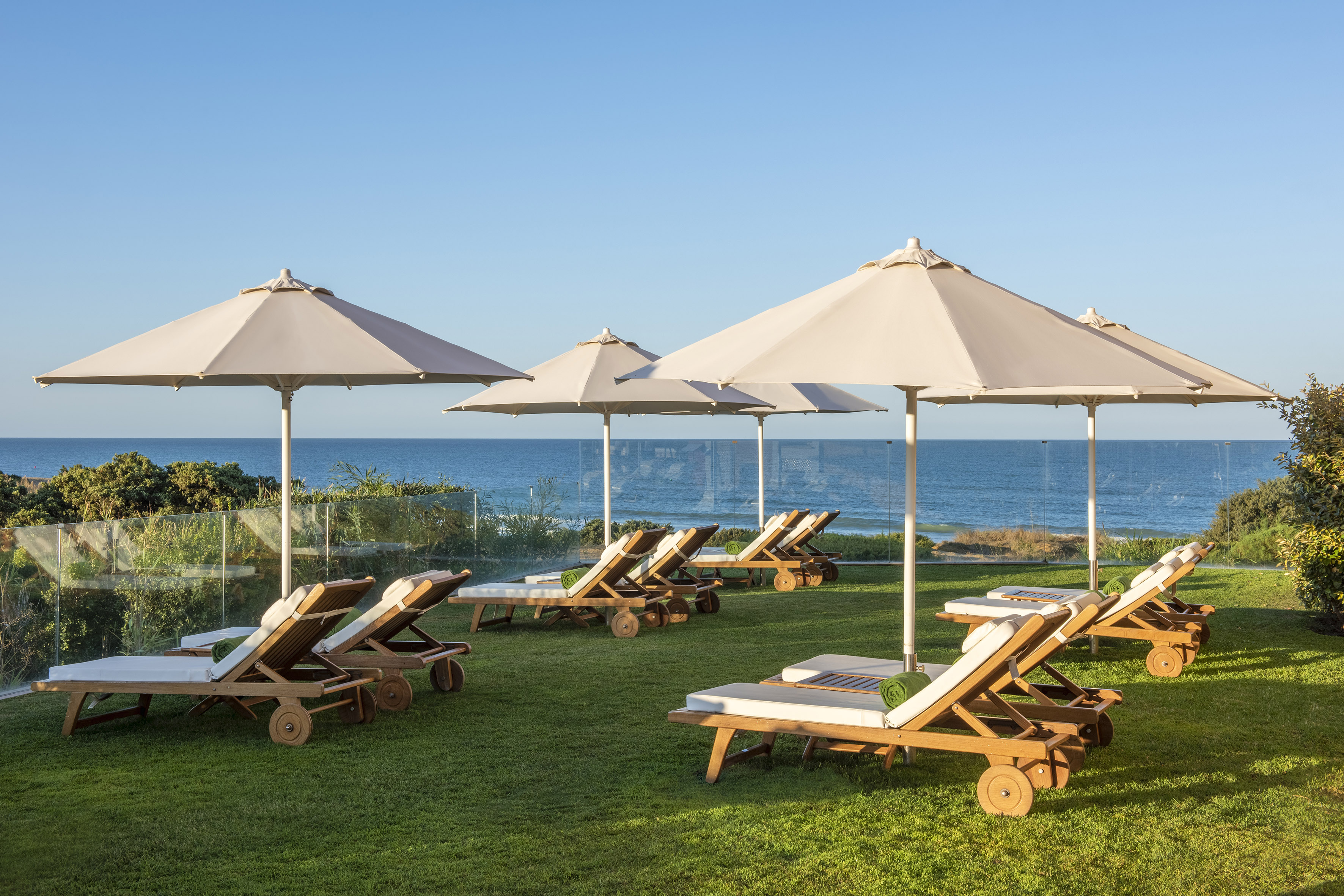 Beach lounge chairs and umbrellas on green lawn with ocean view.
