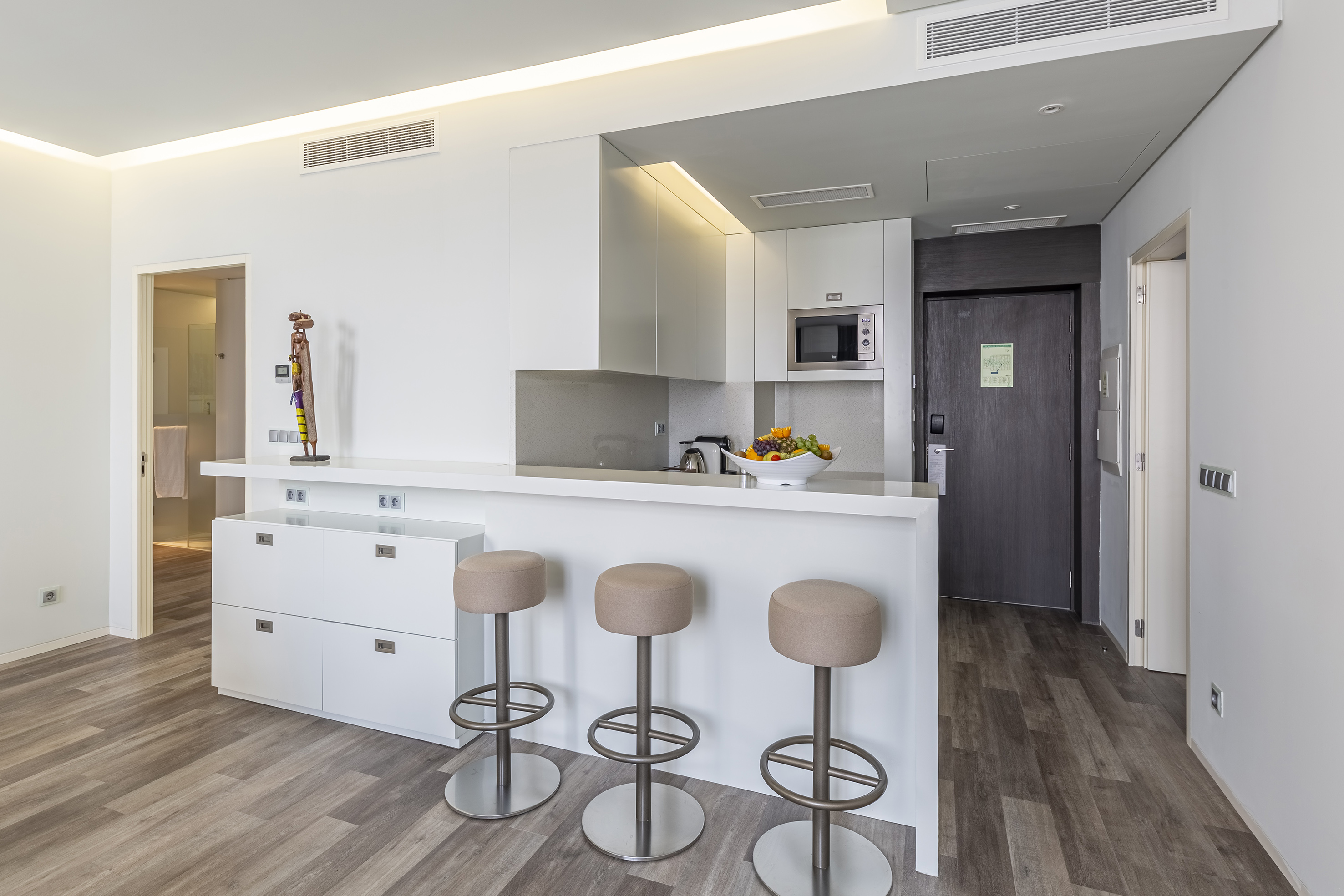 Modern apartment kitchen with white cabinets, island bar, three stools, wood floor.
