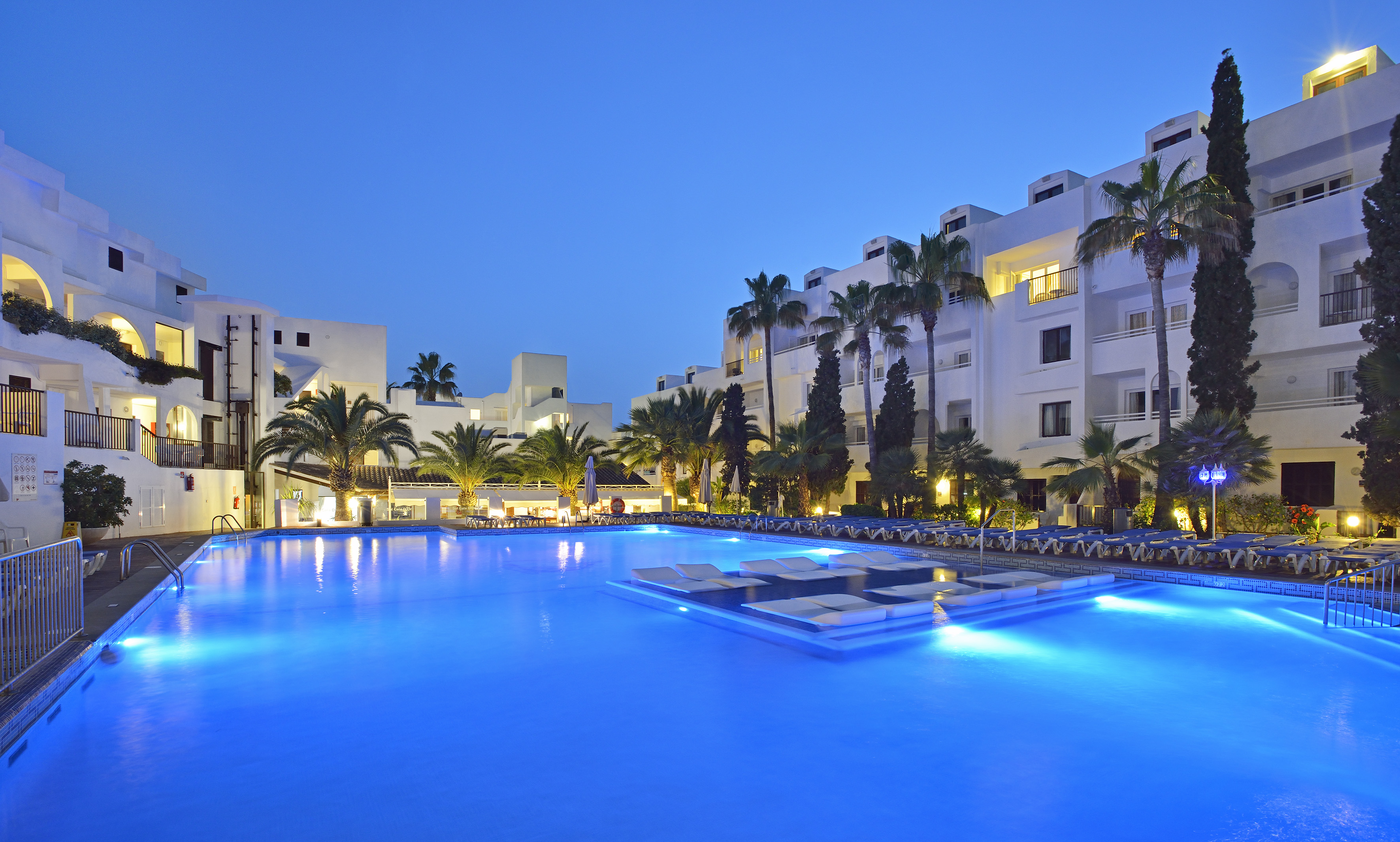 a pool with lounge chairs and palm trees in front of a hotel