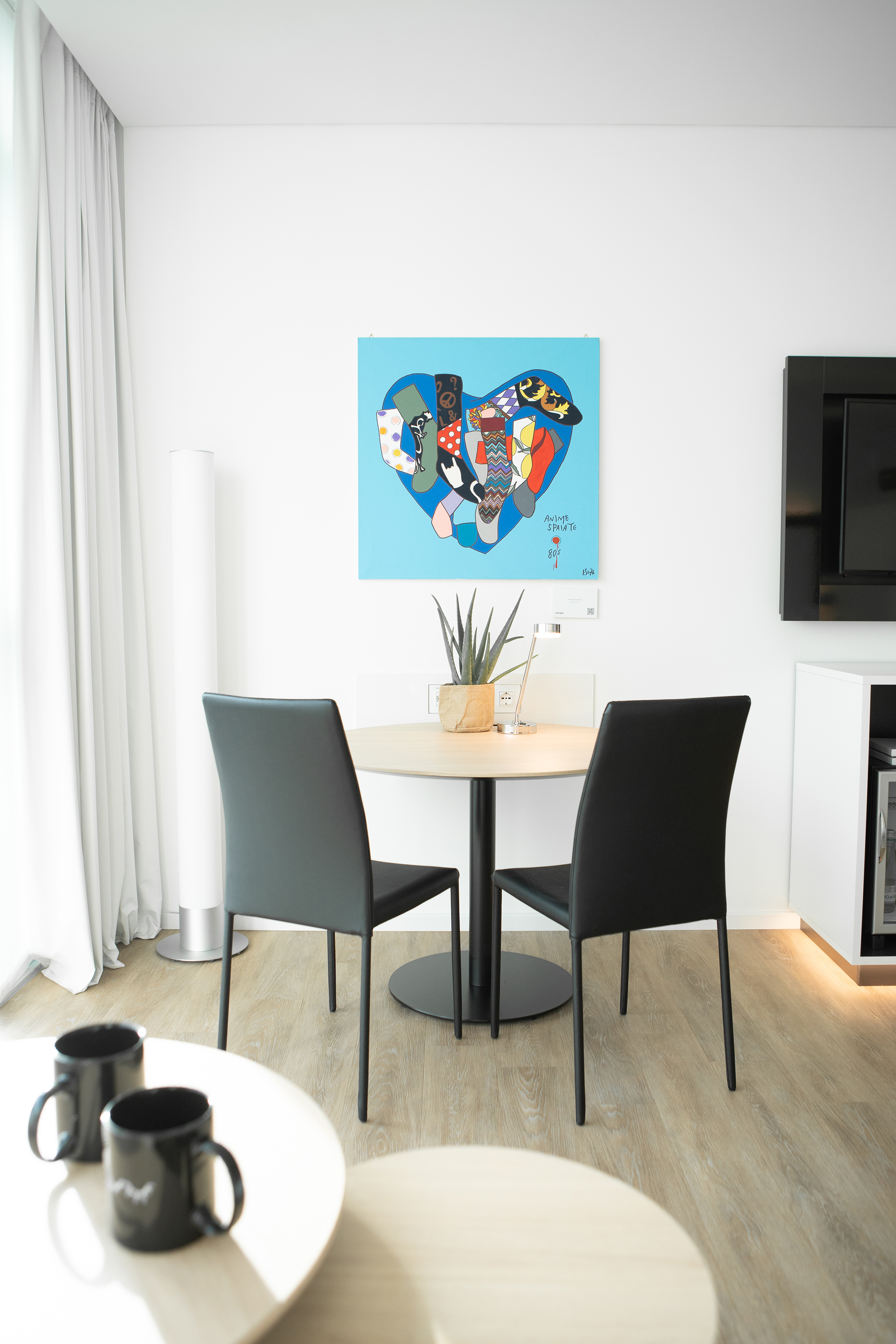 Modern dining area with round table, two black chairs, and colorful heart sock art.