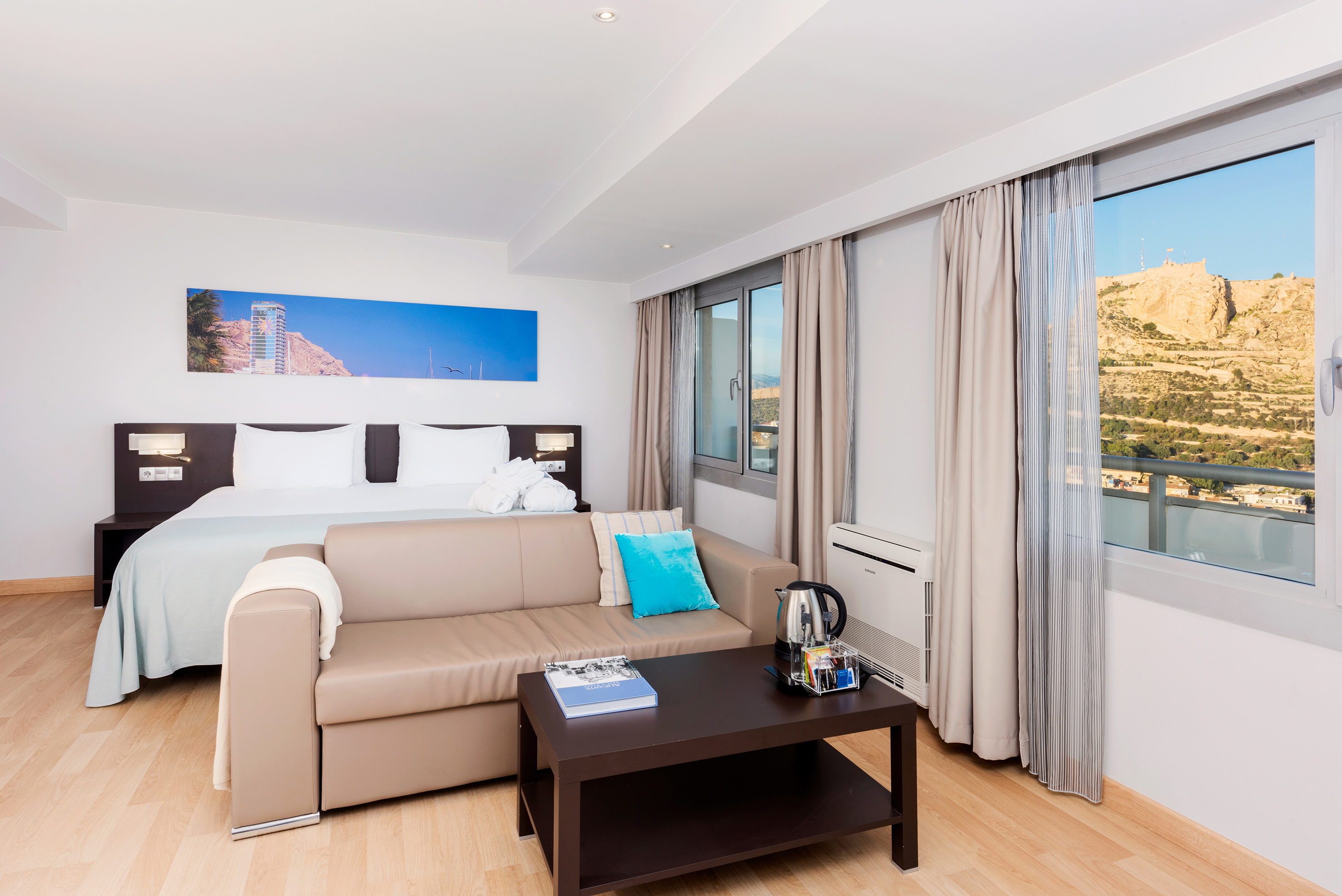 Hotel room with bed, sofa, coffee table, and scenic mountain view.