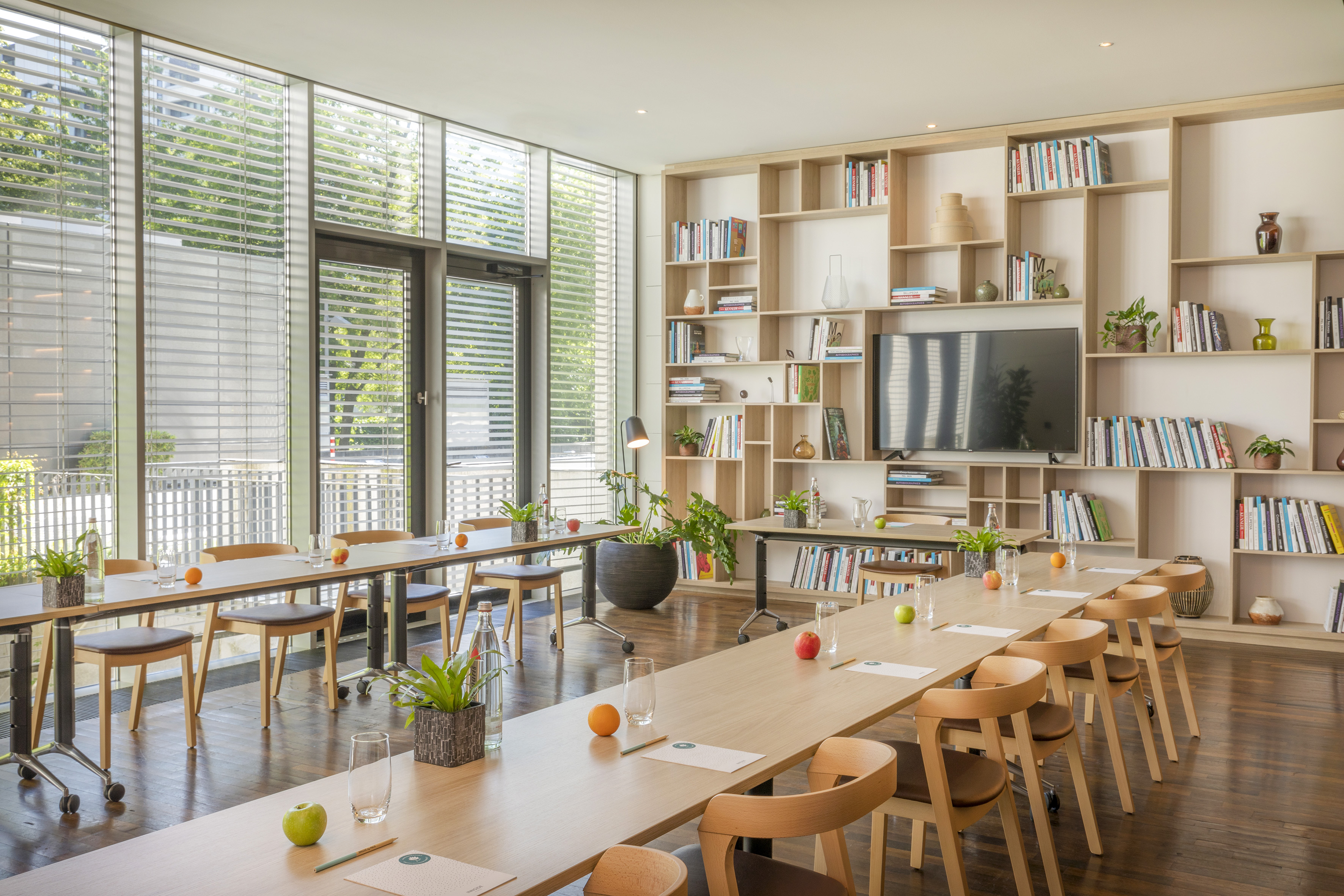 Modern meeting room with wooden tables, large windows, and built-in bookshelf.