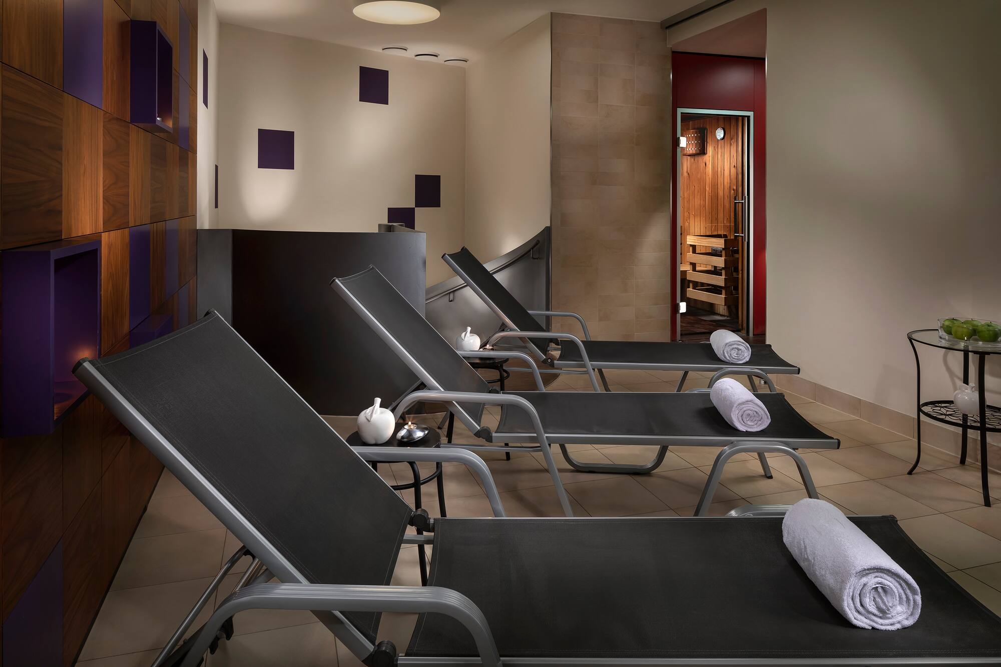 Wellness spa relaxation room with lounge chairs, rolled towels, and sauna.