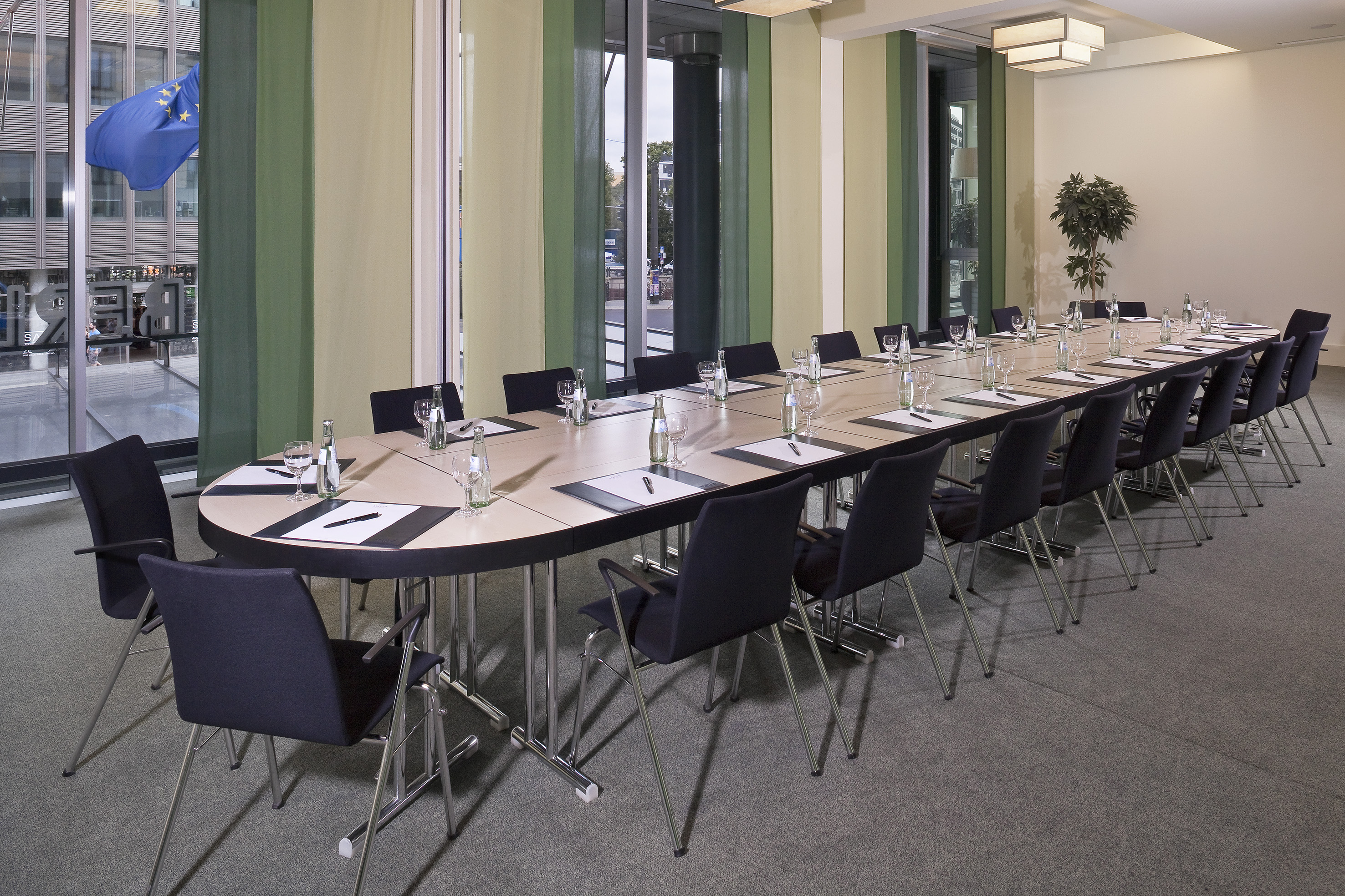 Conference room with oval table, chairs, refreshments, and EU flag outside.