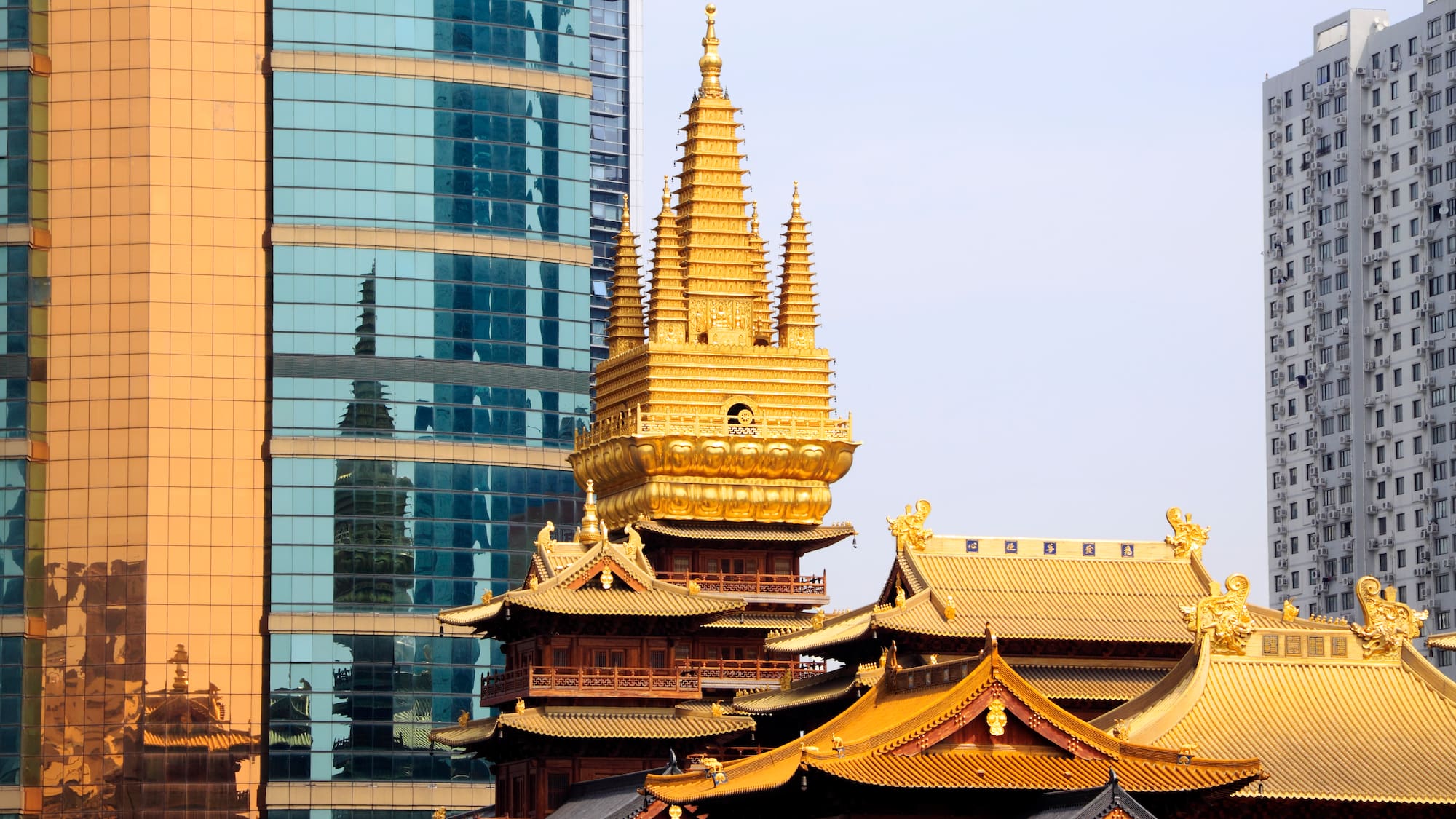 a gold pagoda with a tall tower in front of a glass building