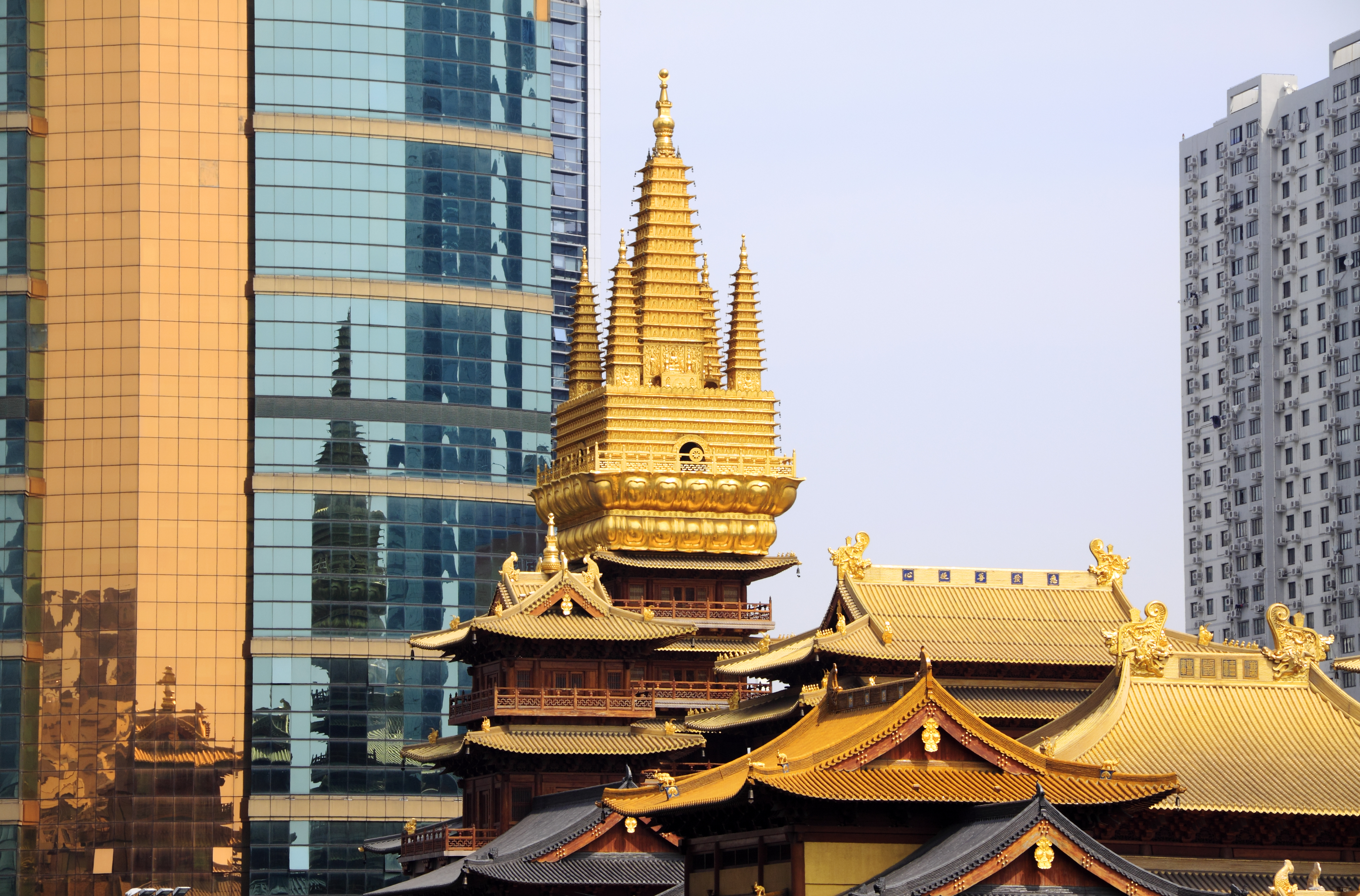 a gold pagoda with a tall tower in front of a glass building