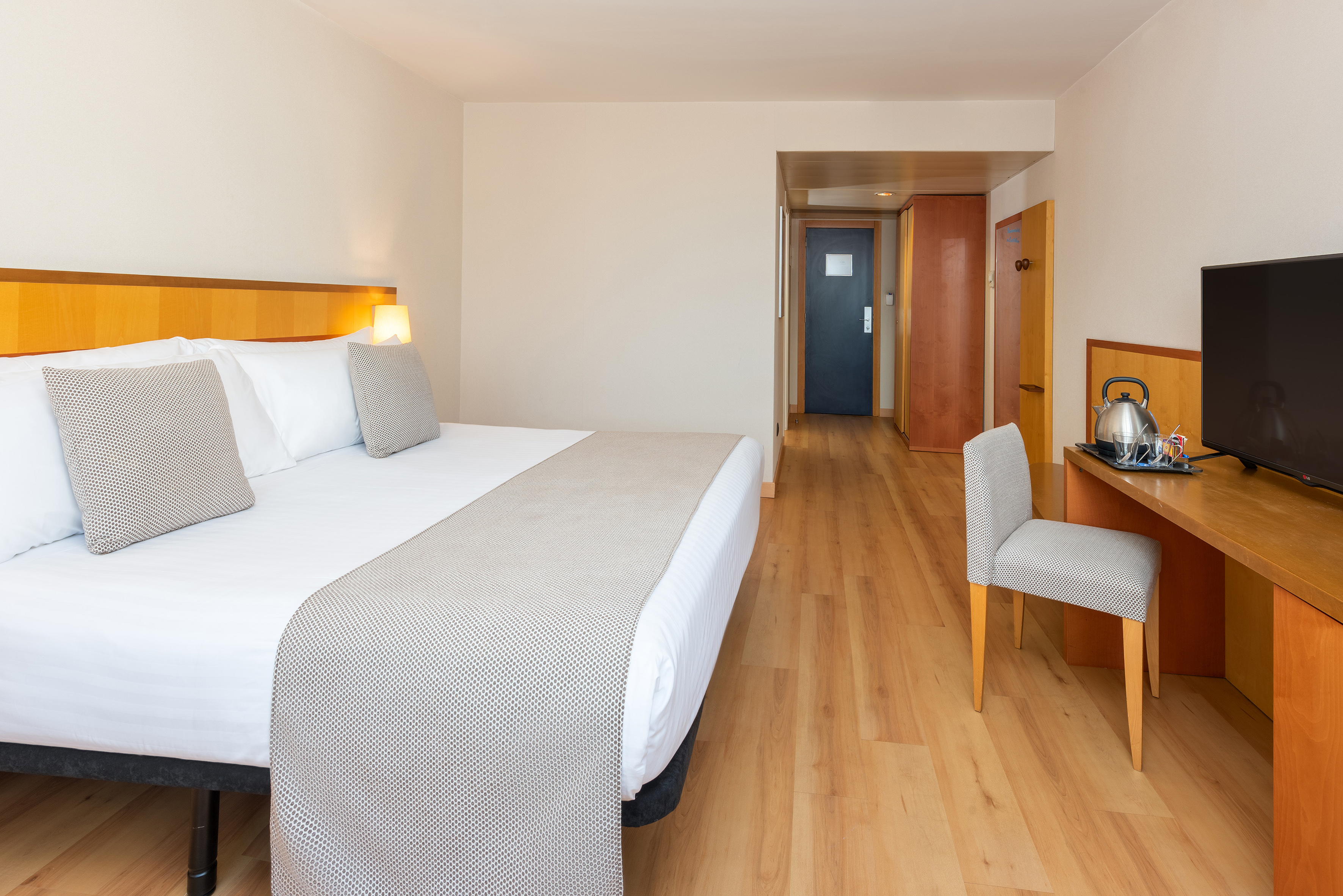 Modern hotel room with comfortable bed, wood floor, desk, and TV.